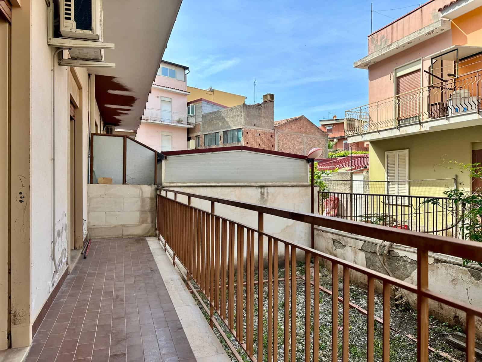 Balcone di un appartamento urbano con ringhiera in metallo e vista su edifici residenziali, in un quartiere di città italiana, sotto un cielo sereno.