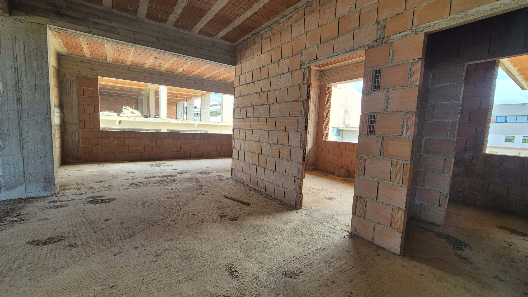 Ampia stanza in costruzione con pareti in mattoni e finestre che lasciano entrare luce naturale, pronta per essere rifinita e personalizzata.