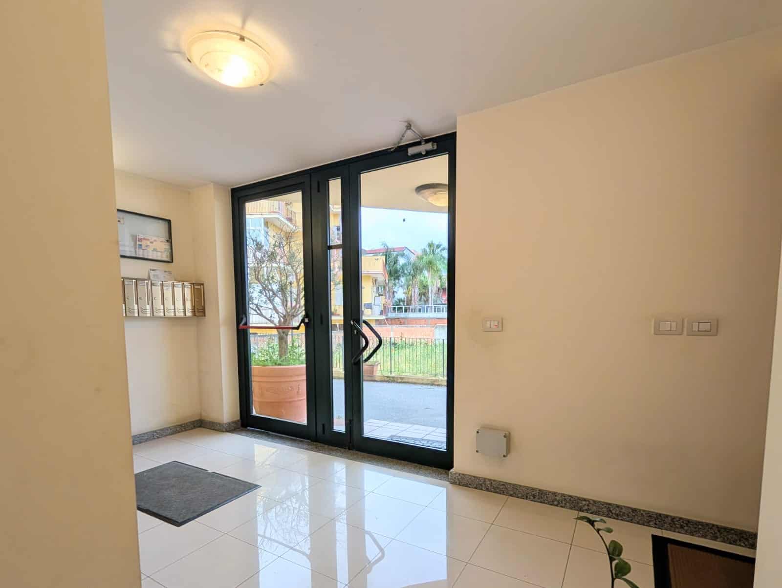 Entrata di un appartamento con porta in vetro e vista sul giardino, ambiente luminoso e moderno, ideale per affitti o vendita immobiliare.