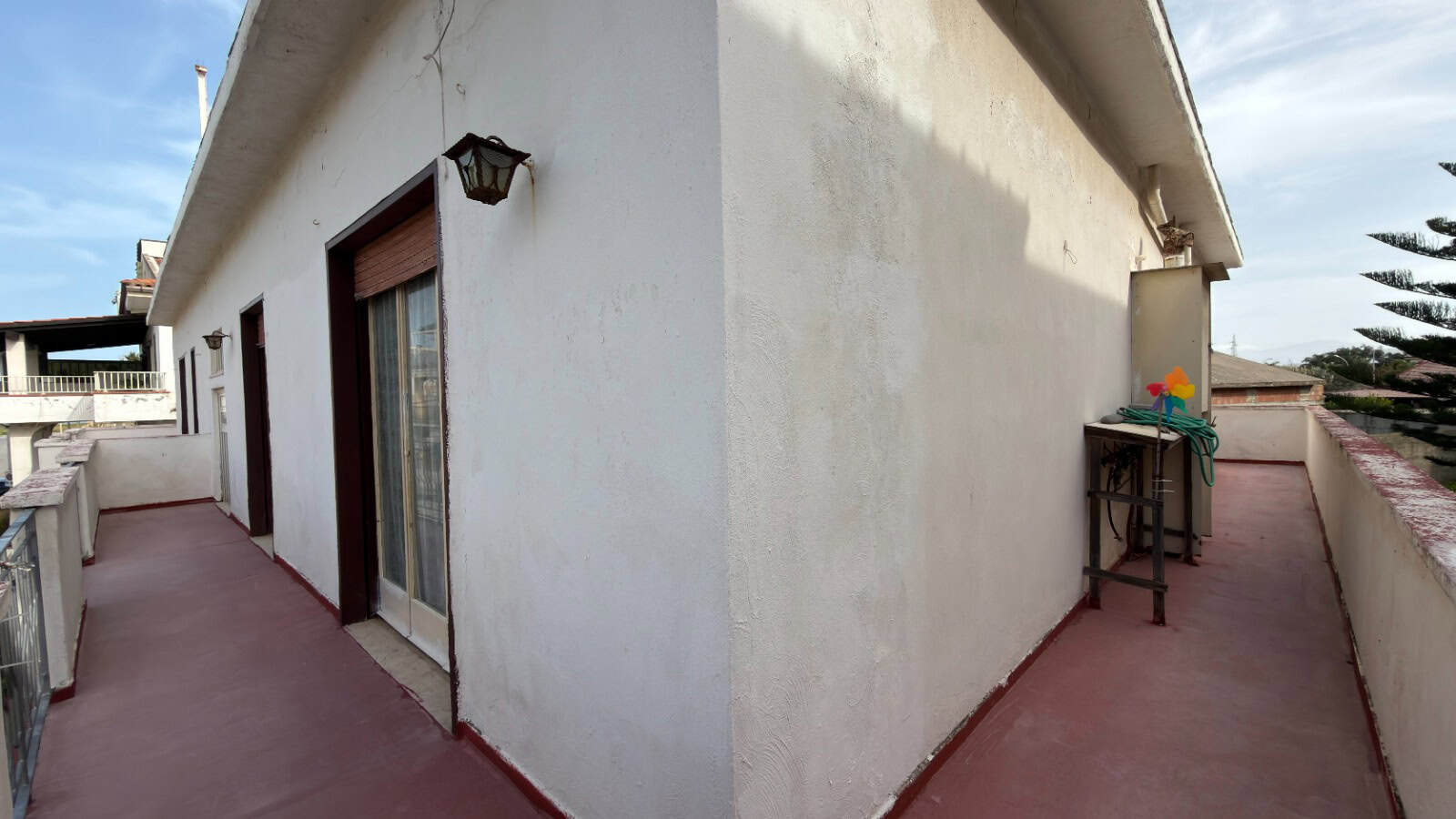 Balcone di un appartamento con pareti bianche, porta finestra e tavolo con ombrellone, ideale per relax e vista panoramica.