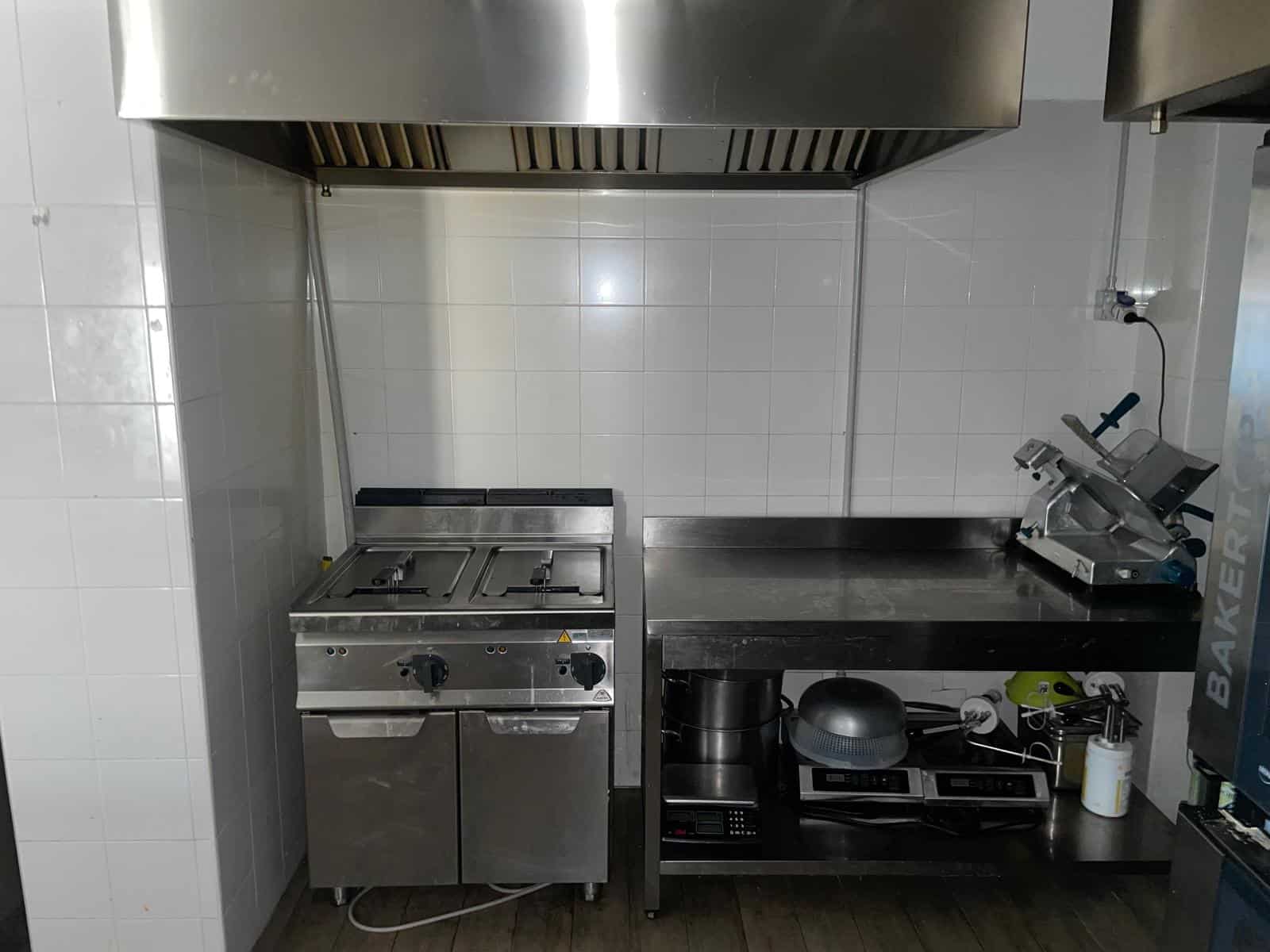 Cucina professionale con attrezzature per la preparazione di cibi, inclusi forni e piani di lavoro in acciaio inox, ideale per ristoranti e cucine commerciali.
