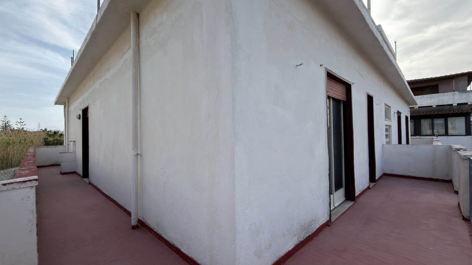Ampia terrazza panoramica su edificio residenziale con vista sul cielo nuvoloso, superficie in cemento e pareti bianche, ideale per relax e socializzazione all'aperto.