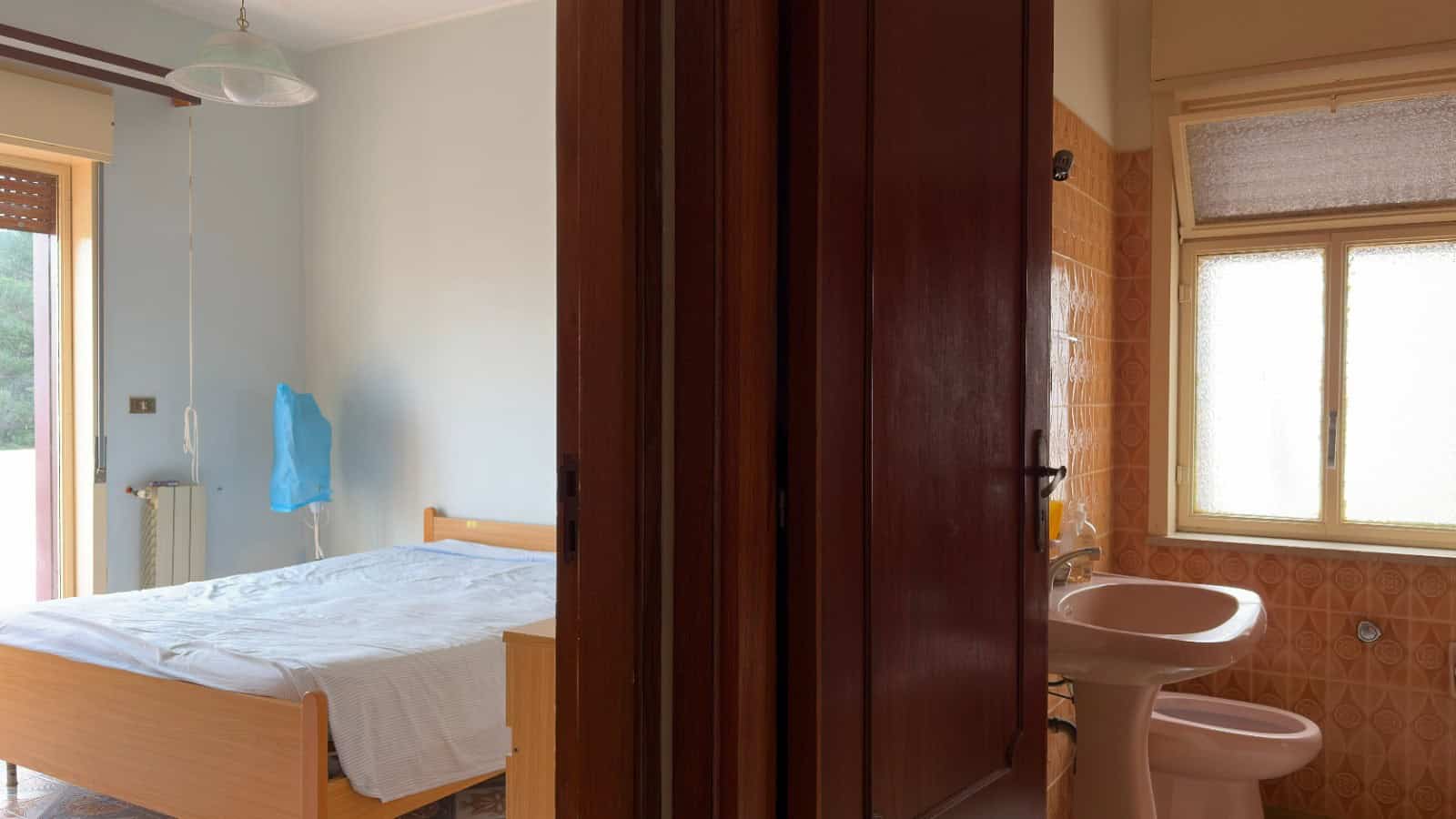Ampia camera da letto e bagno con finestra, arredamento semplice e funzionale, ideale per affitti turistici o residenziali, rappresentando un esempio di proprietà immobiliare di NextCasa.