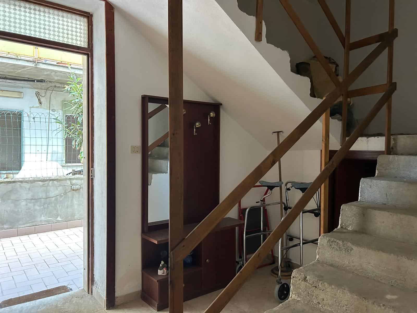 Interno di una scala in cemento e legno con accessori per disabili, ingresso di una casa a NextCasa, soluzione abitativa accessibile e moderna.