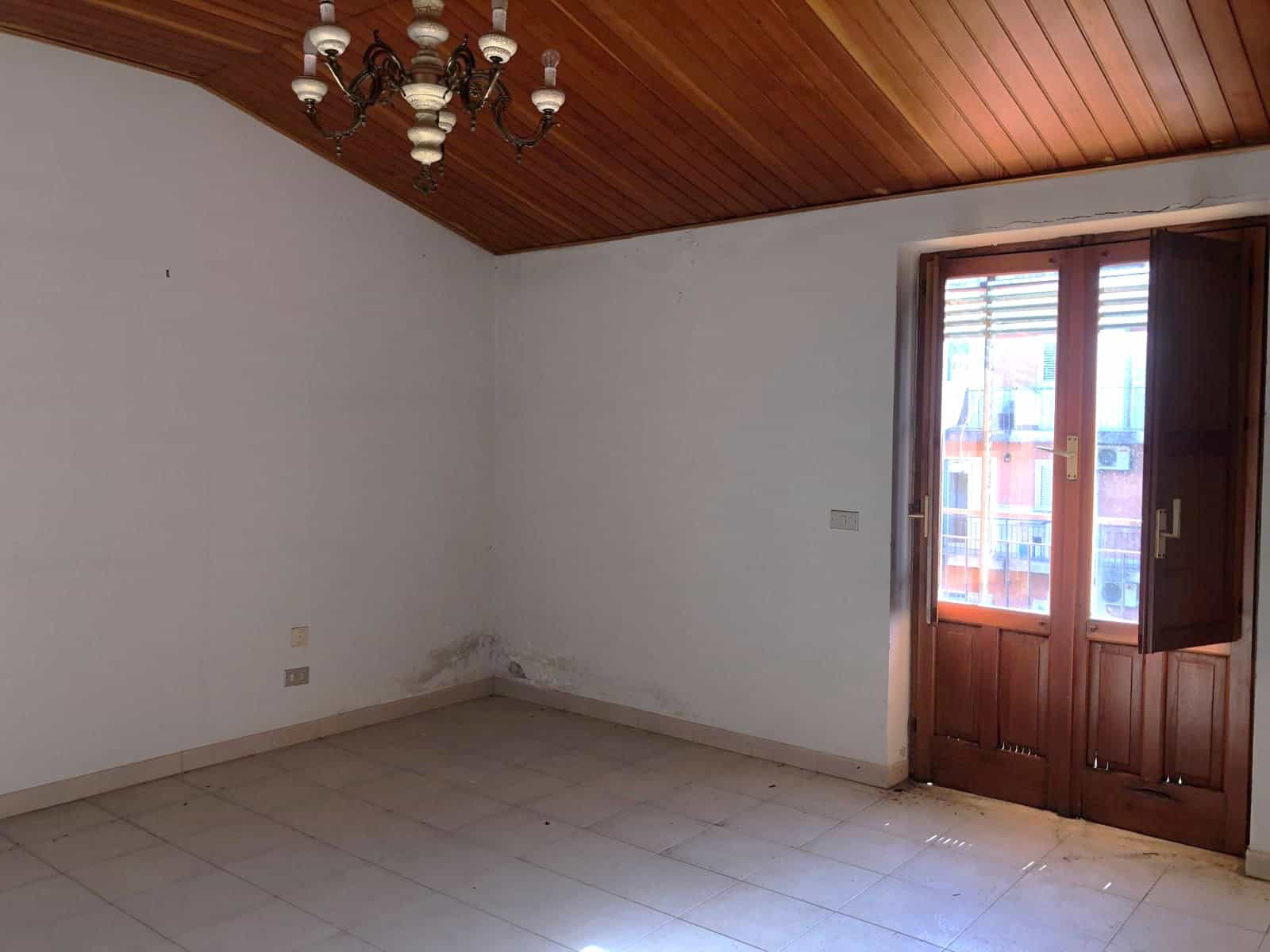 Il soffitto in legno e la porta finestra in legno massiccio in una stanza vuota con pareti bianche e pavimento in piastrelle, pronta per essere arredata.