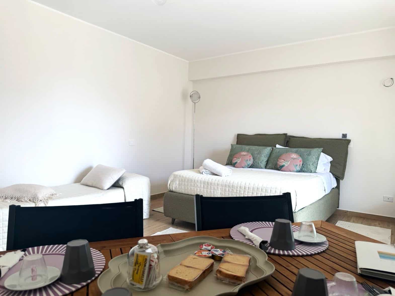 Una stanza da letto moderna e luminosa con letto matrimoniale, sedie nere, e un tavolo con snack e bevande, ideale per affitti di case vacanza o appartamenti di lusso.