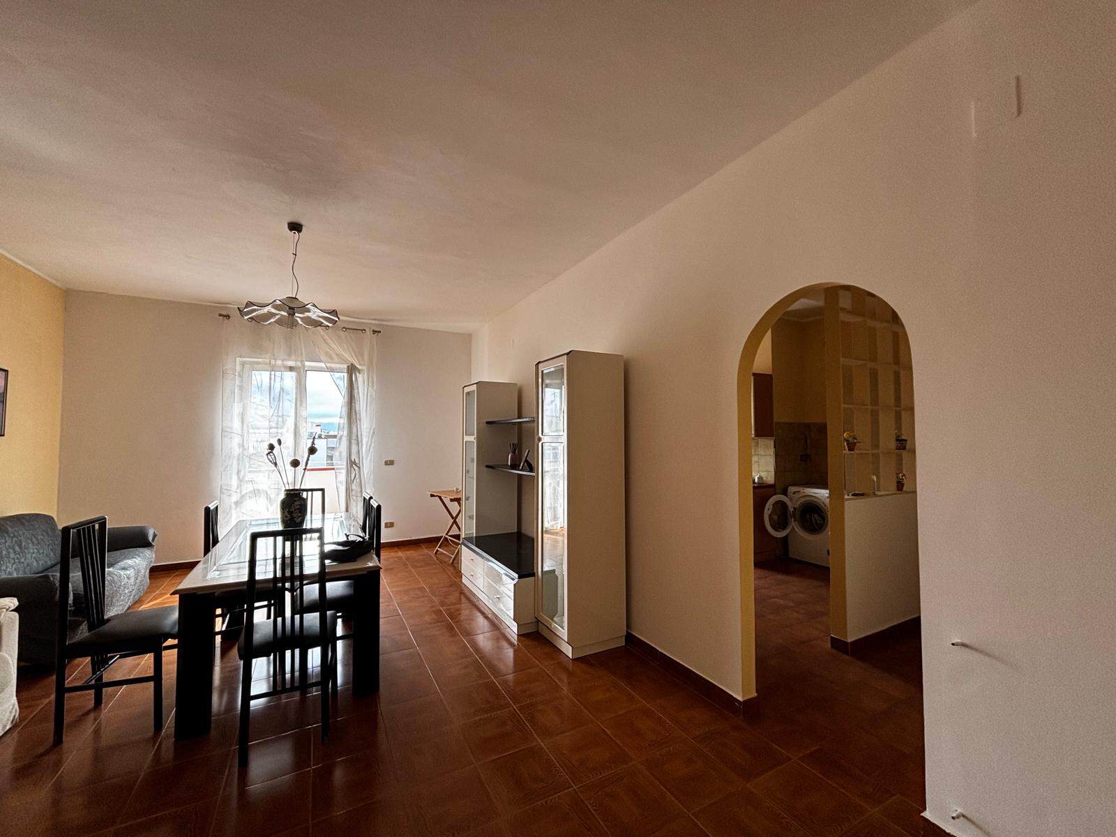 Spazio soggiorno luminoso con zona pranzo, arredamento moderno, pareti chiare e pavimento in piastrelle, vista sulla finestra con tende leggere, ingresso alla cucina e lavanderia.