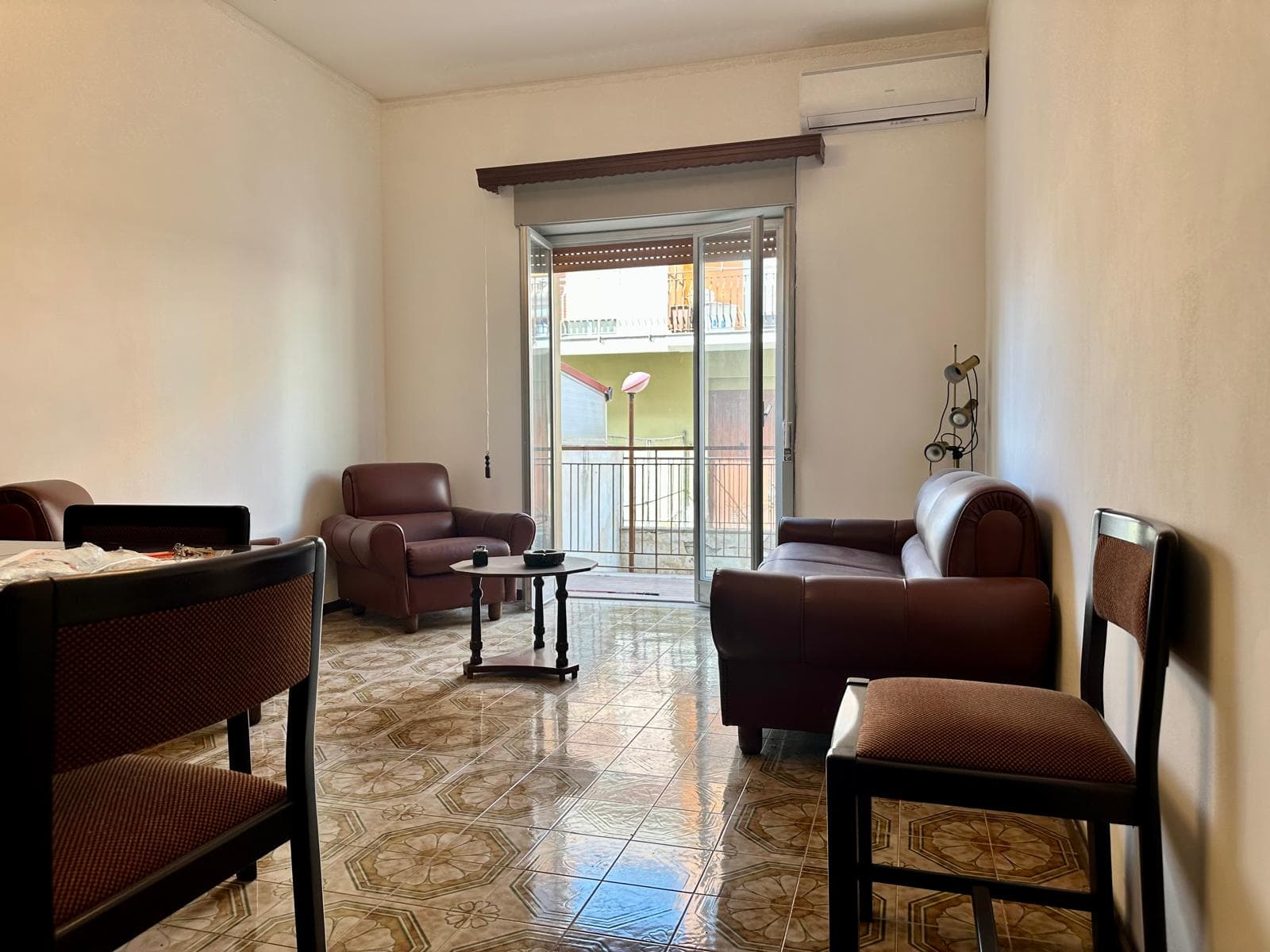 Soggiorno luminoso con divani in pelle e tavolino, vista su balcone con apertura verso l'esterno, arredamento accogliente e spazioso, ideale per relax e incontri familiari.