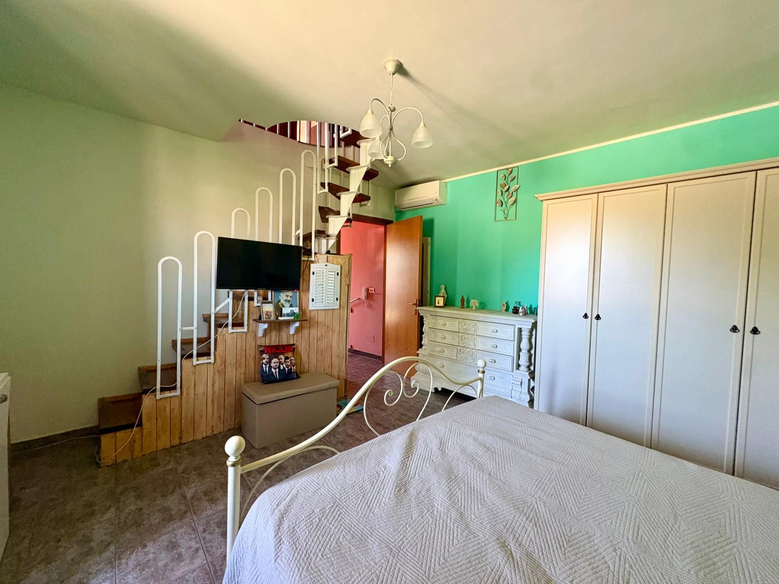Elegante camera da letto con letto in ferro battuto, armadio a muro e pareti colorate, illuminata da luce naturale, ideale per soggiorno confortevole e stile moderno.