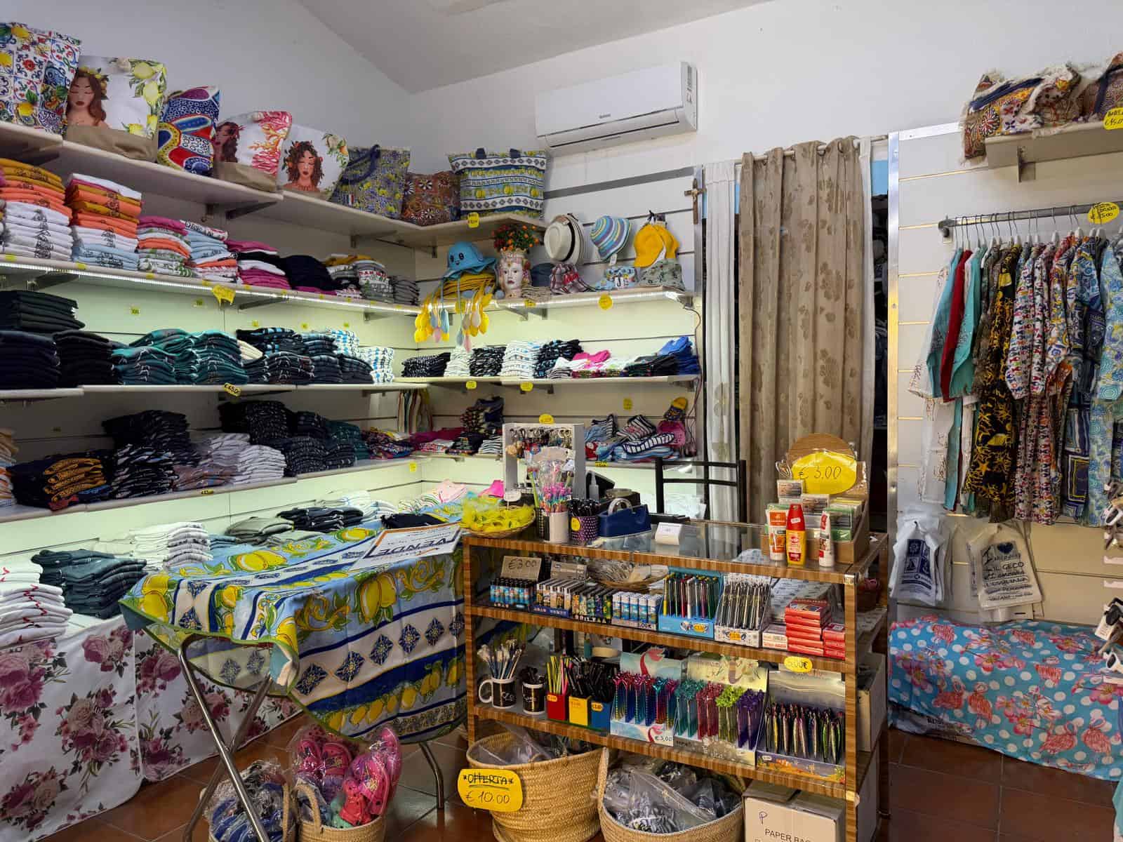 Tende, tessuti e accessori per la casa in un negozio di biancheria e decorazioni, con scaffali pieni di prodotti colorati e organizzati, ambiente luminoso e accogliente.