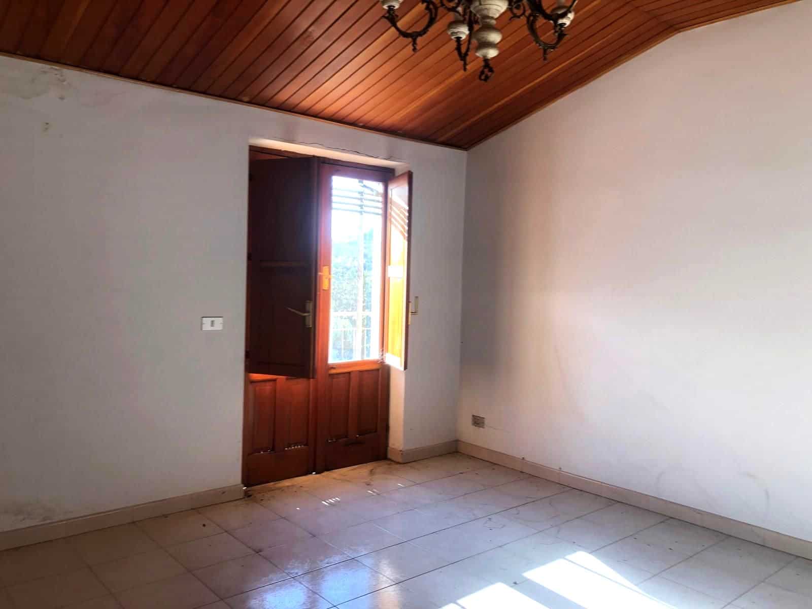 Finestra in una stanza vuota con pareti bianche, pavimento in piastrelle e soffitto in legno, luce naturale che entra dalla finestra.