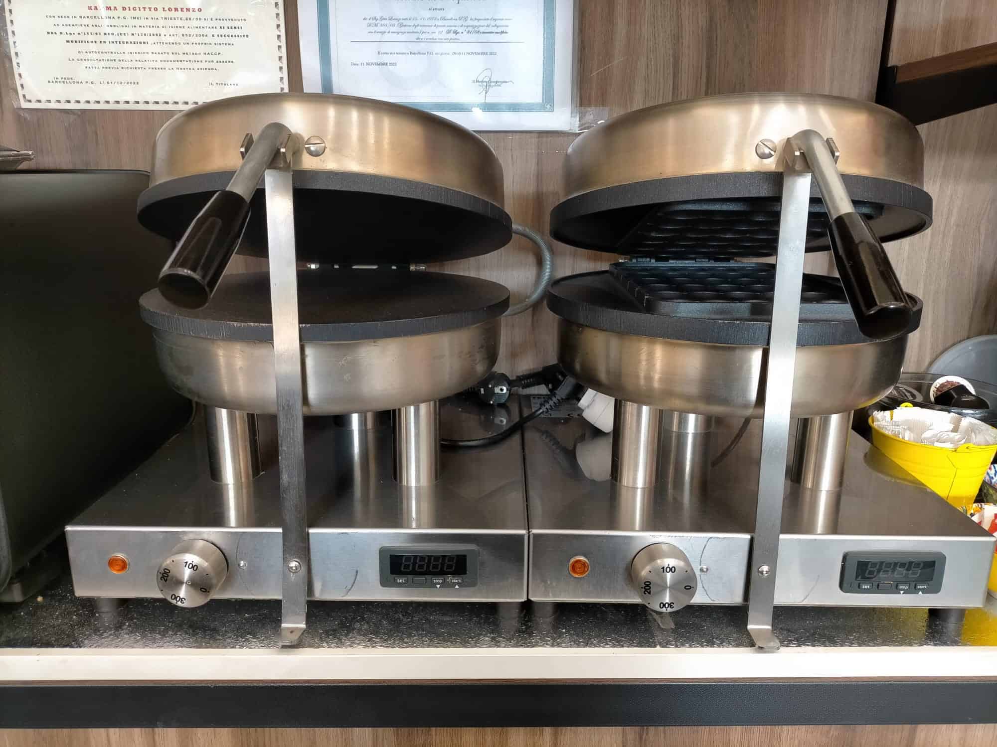 Ferro da waffle professionale in acciaio inox con due piastre riscaldanti, ideale per preparare dolci croccanti e fragranti in caffetterie o ristoranti.