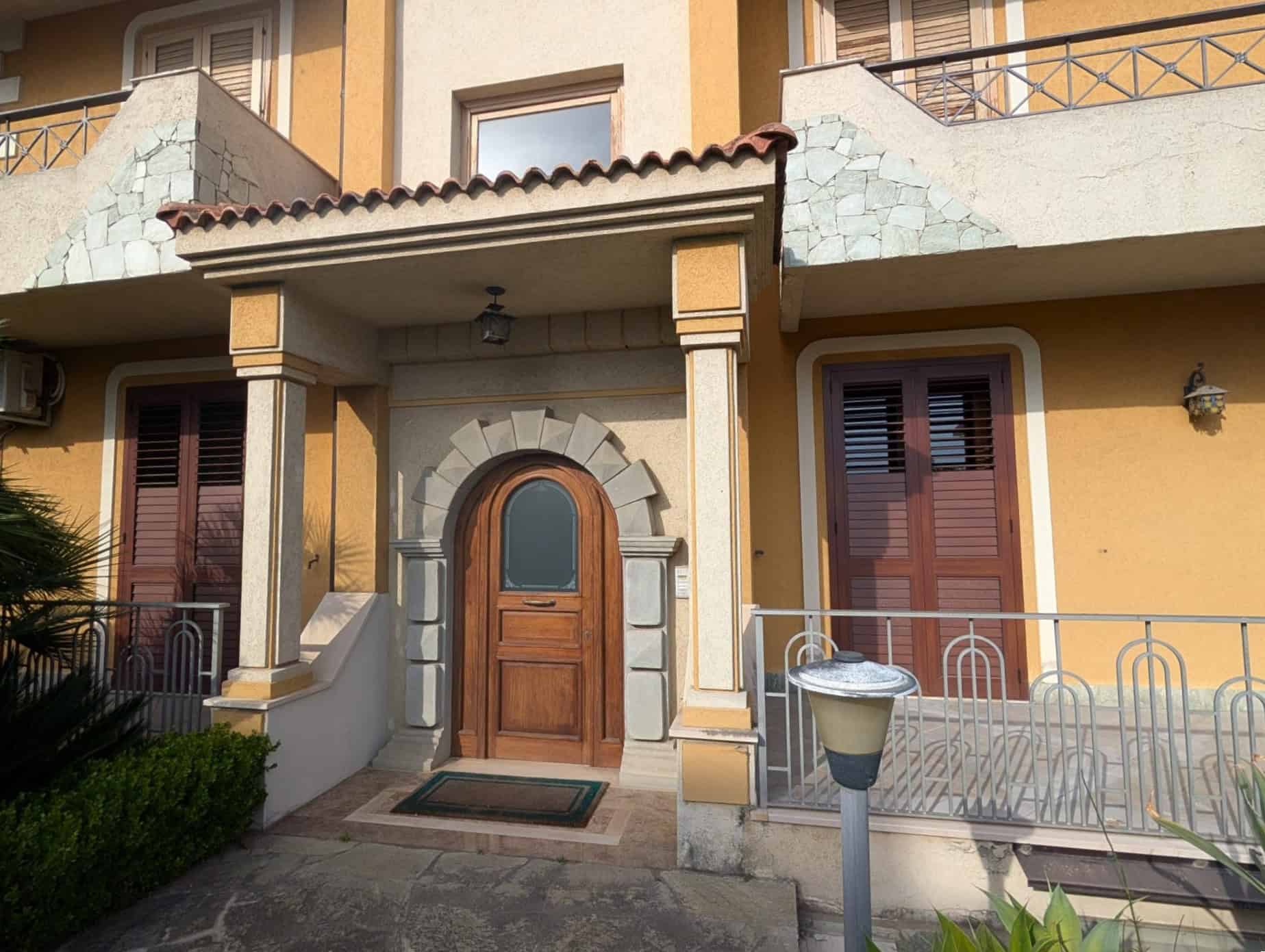 Ampia immagine di una casa con ingresso in legno, dettagli architettonici in pietra e balconi con ringhiere in metallo, in stile mediterraneo, perfetta per annunci immobiliari e ristrutturazioni.
