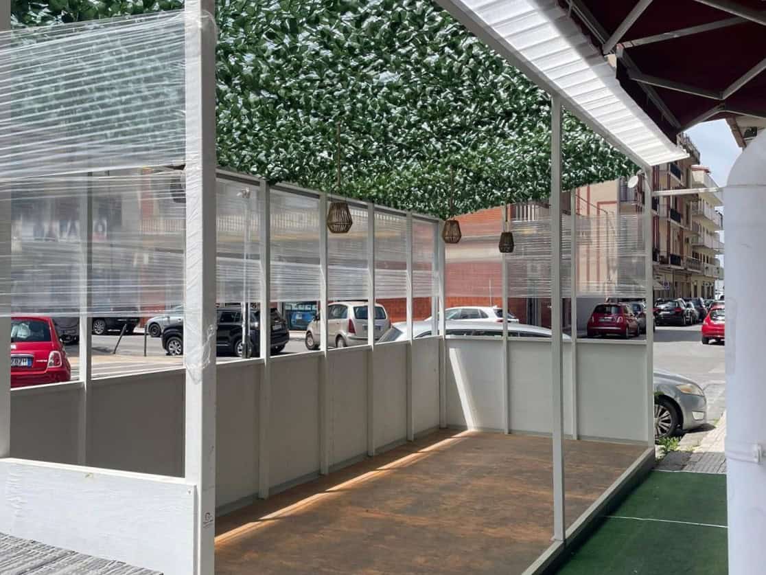 Ampia area esterna coperta con tetto verde, ideale per eventi o relax, con pavimentazione in legno e vista sul parcheggio e le auto circostanti, in un contesto urbano moderno.
