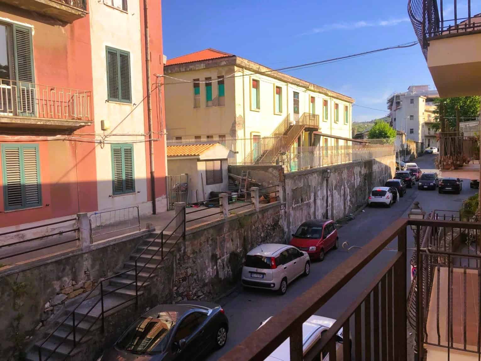 Vista di un quartiere residenziale con edifici colorati e auto parcheggiate lungo la strada, in una giornata soleggiata.