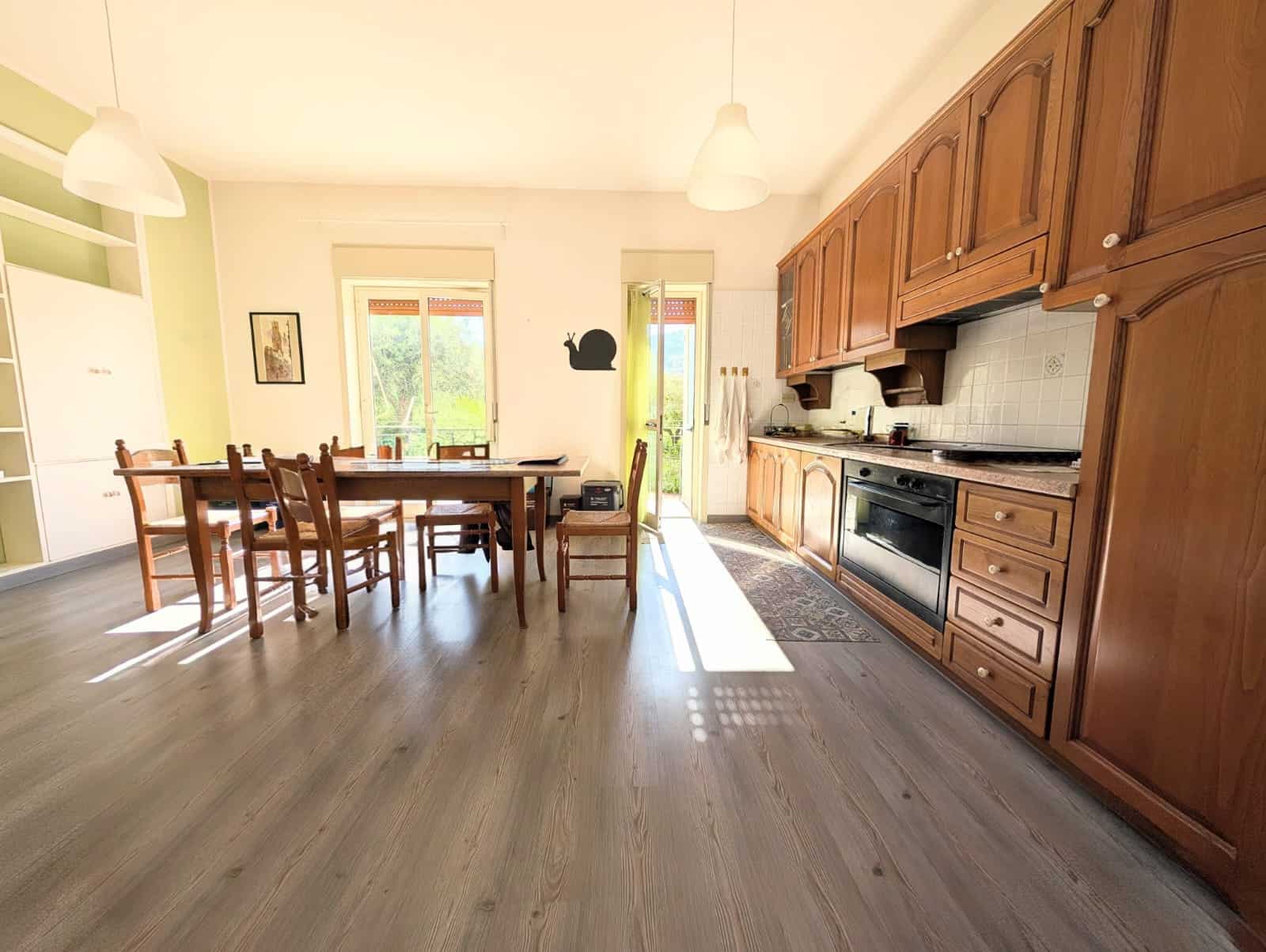 Pannello solare sul tetto di una cucina moderna con mobili in legno e grande tavolo da pranzo, ambiente luminoso e accogliente, ideale per famiglie e cene conviviali.