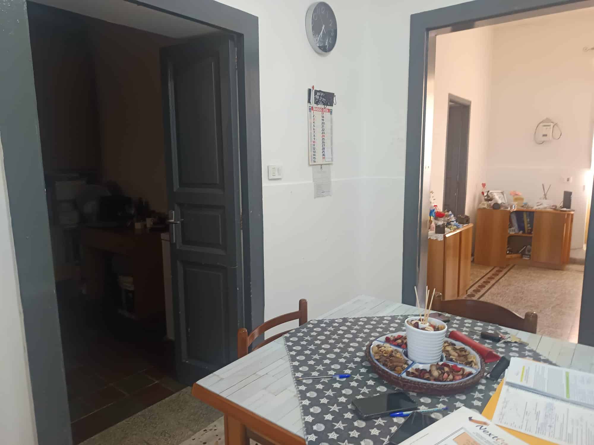 Interno di una casa con tavolo da pranzo decorato, cucina visibile sullo sfondo, ambiente luminoso e accogliente, ideale per vivere momenti conviviali e familiari.