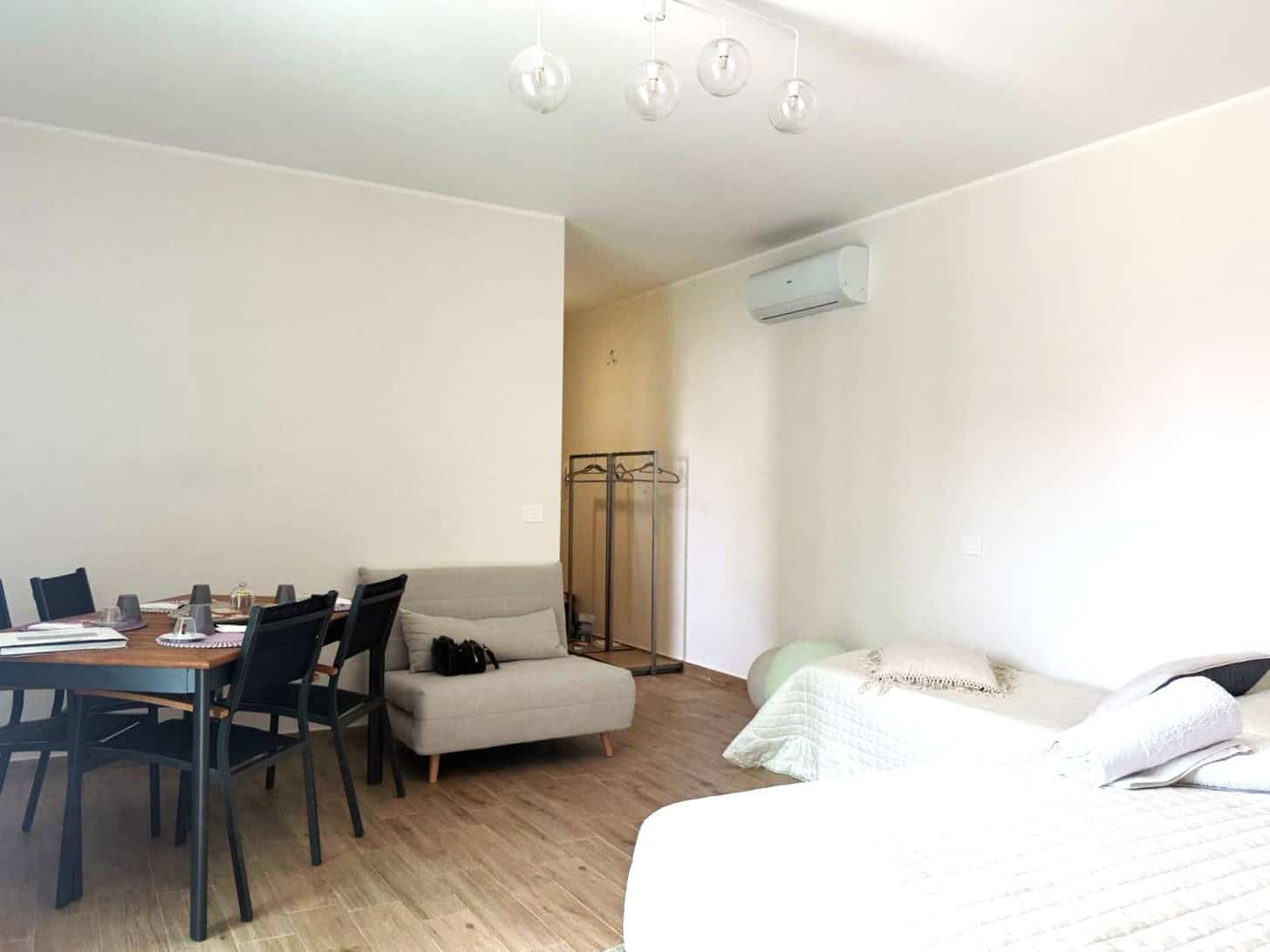 Interno di un appartamento moderno con zona soggiorno e camera da letto, arredato con stile minimalista e illuminazione naturale, ideale per affitti a breve termine o residenze permanenti.