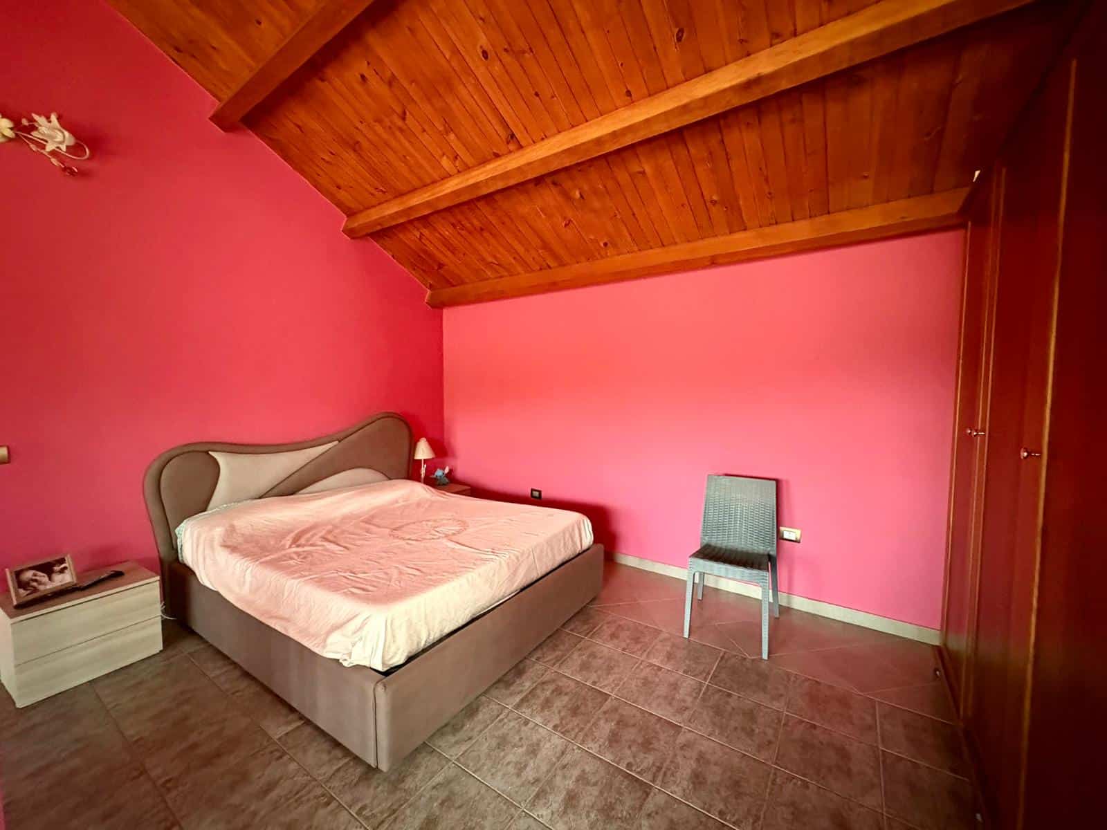 Il letto matrimoniale in una camera con pareti rosa e soffitto in legno, arredamento semplice e accogliente, ideale per soggiorni confortevoli.