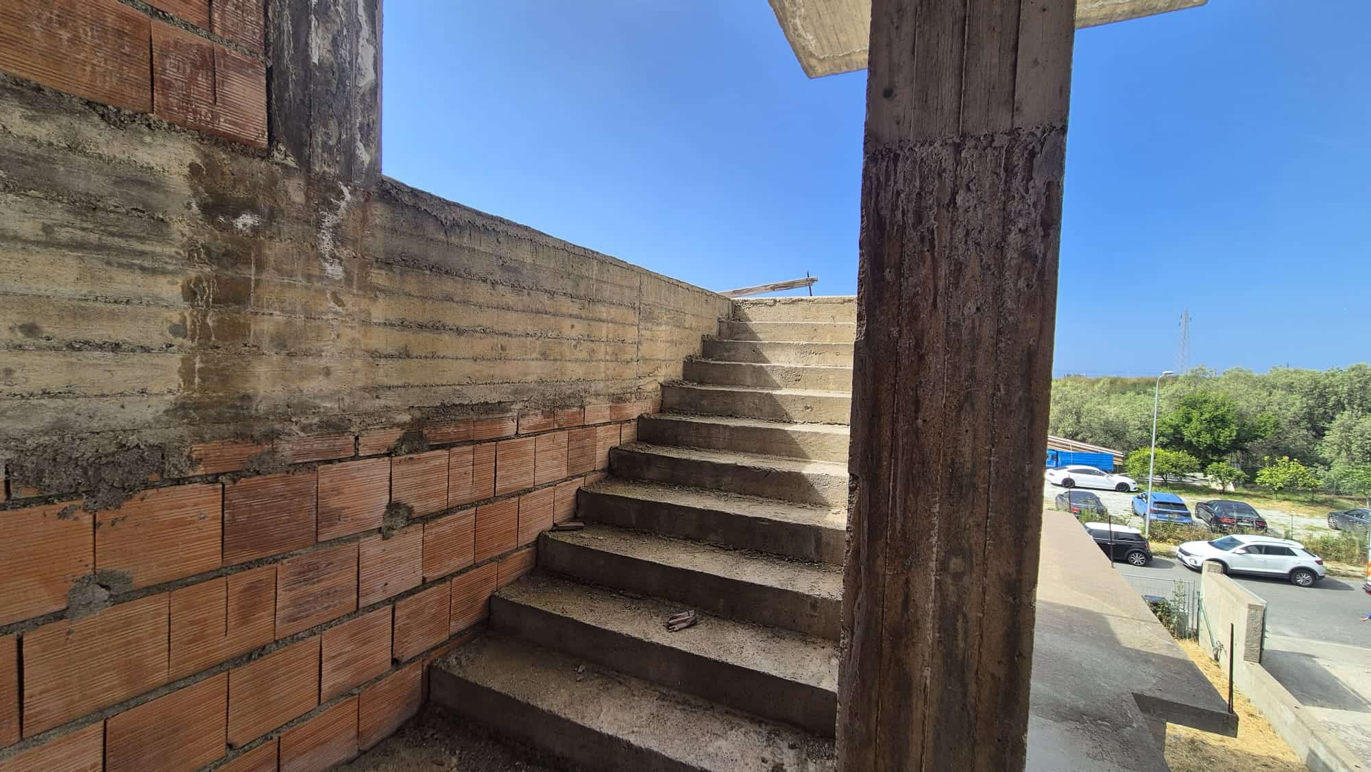 Scale in cemento con ringhiera in un edificio in costruzione, vista verso il cielo e il paesaggio circostante, rappresenta un'area di sviluppo immobiliare NextCasa.