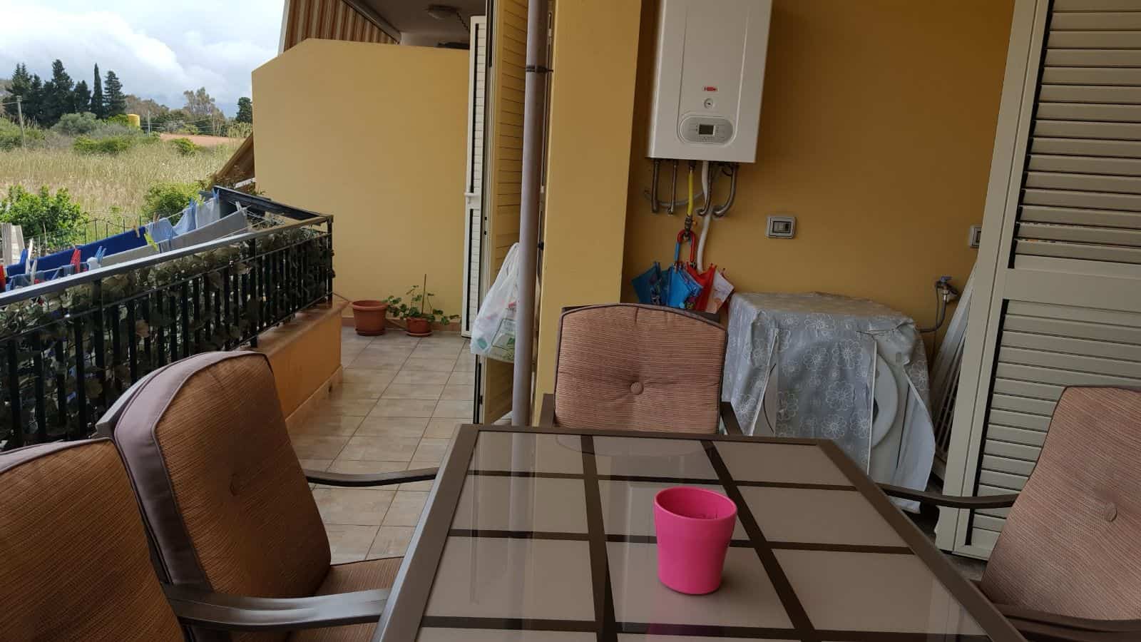 Panchina e tavolo da esterno su balcone con vista su campagna verde e cielo nuvoloso, ambiente accogliente e rilassante.