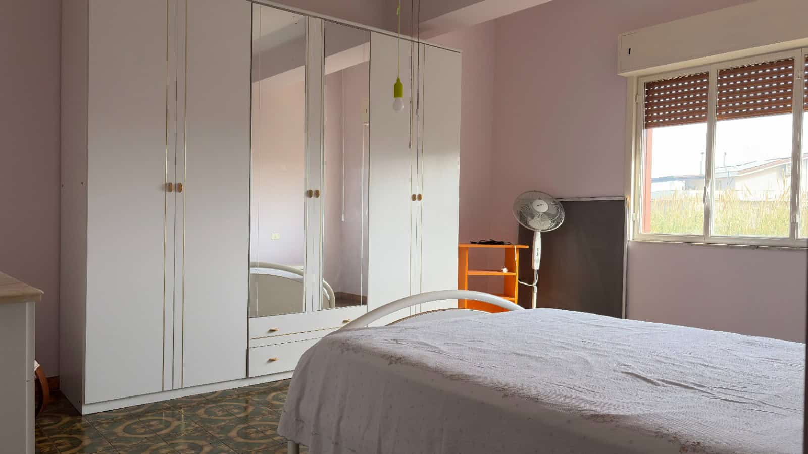 Ampia camera da letto con armadio a muro bianco e finestra che lascia entrare luce naturale, arredamento semplice e funzionale, ideale per ambienti residenziali moderni.