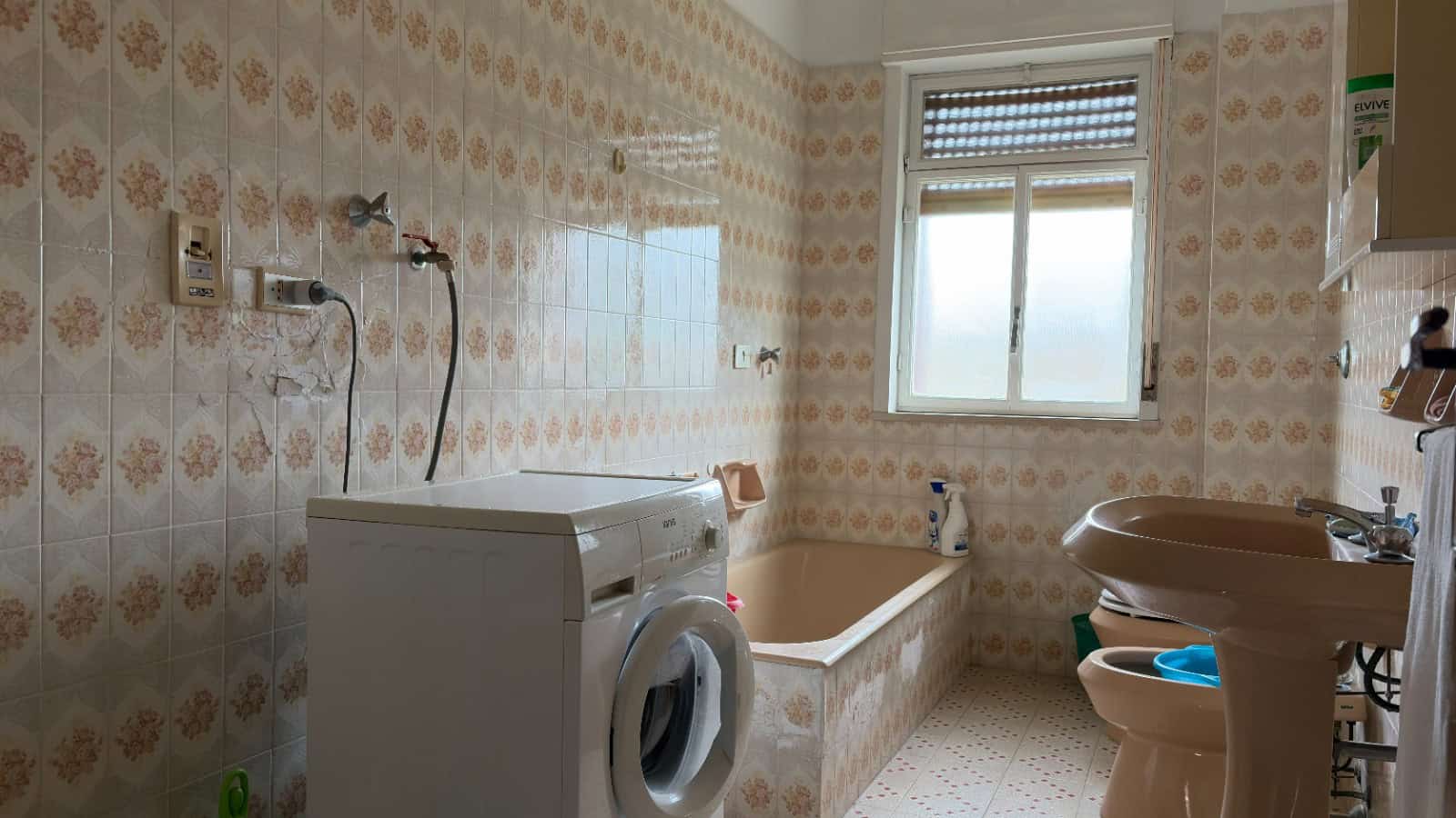 Lavatrice e vasca da bagno in un bagno con piastrelle vintage e finestra luminosa.