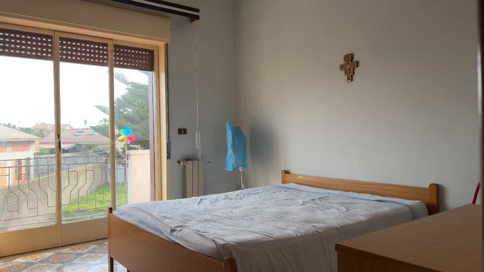 Letto matrimoniale in una camera luminosa con grande finestra che dà su un giardino esterno, ambiente accogliente e ben arredato, ideale per soggiorni confortevoli e rilassanti.