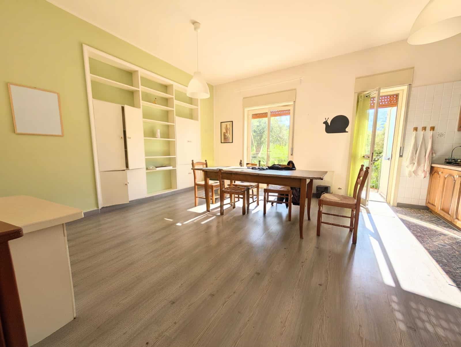 Ampia zona pranzo e soggiorno in appartamento luminoso con grandi finestre e accesso al balcone, arredato con tavolo e sedie, ideale per vivere in comfort e stile.