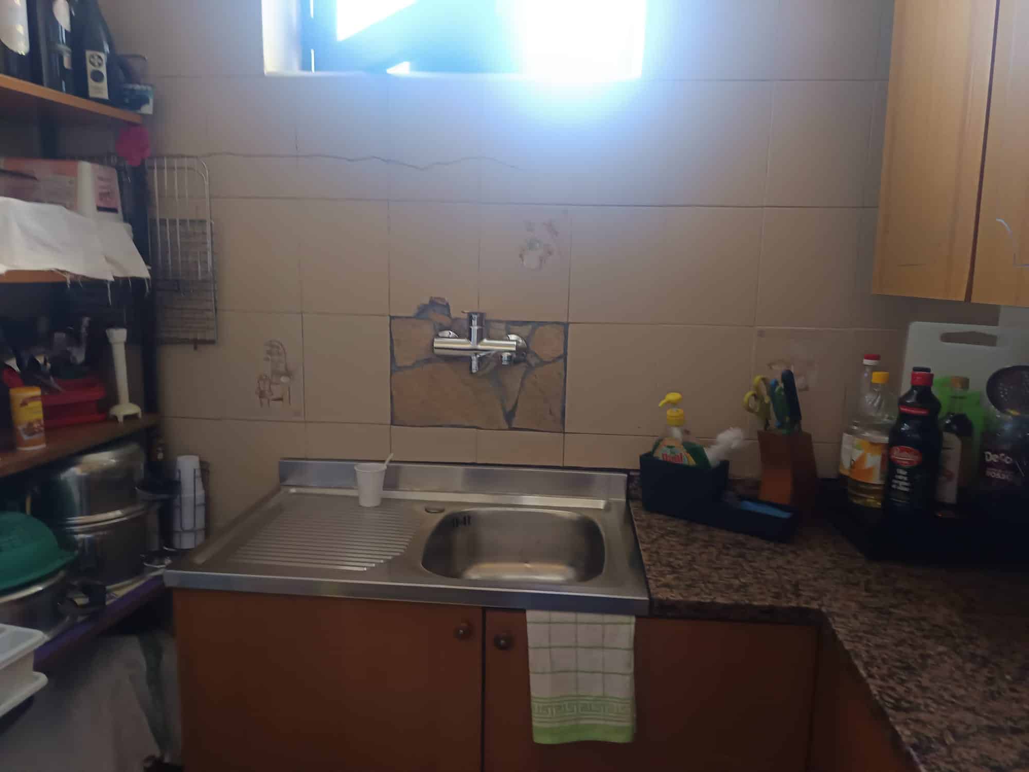 Lavandino da cucina con ripiano in granito, scaffali e utensili in un ambiente domestico ben organizzato, illuminato dalla luce naturale proveniente dalla finestra.