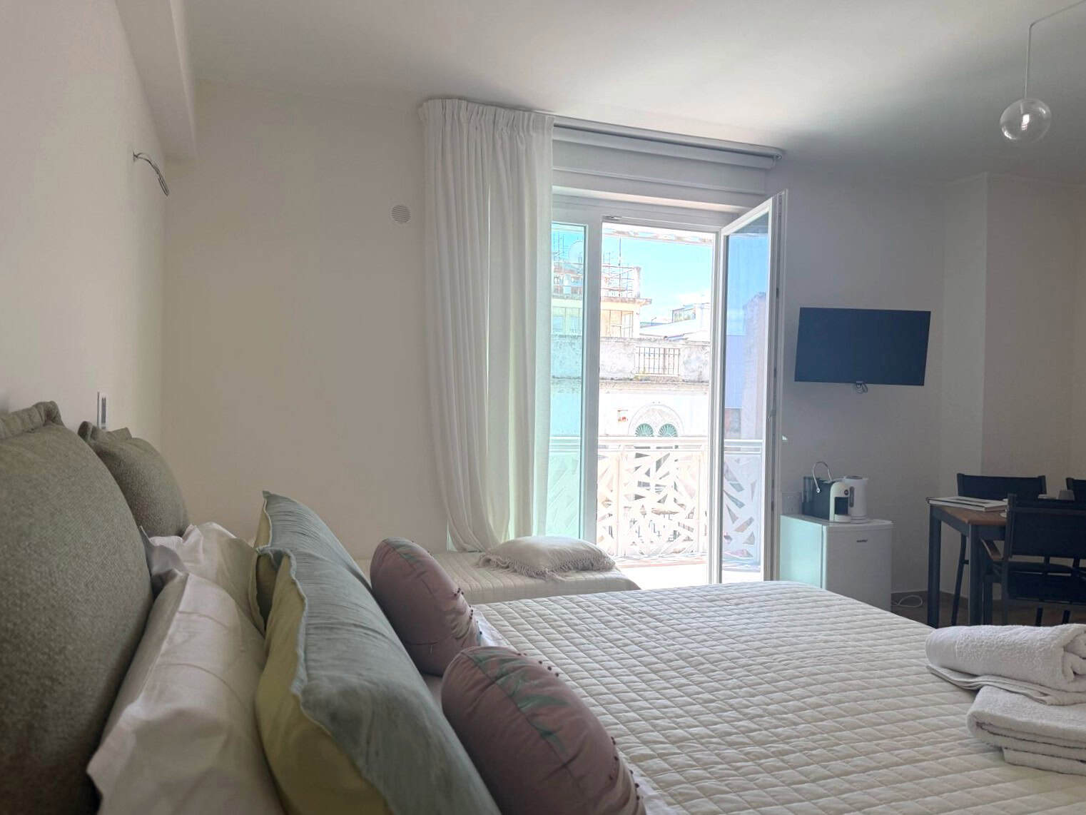 Ampio soggiorno con balcone e vista sulla città, arredato con letto matrimoniale, divano e TV, ideale per soggiorni confortevoli e rilassanti.