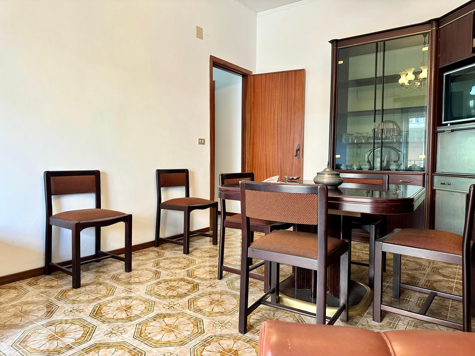 Sedie e tavolo da pranzo in legno in una stanza luminosa con pavimento in piastrelle decorato.