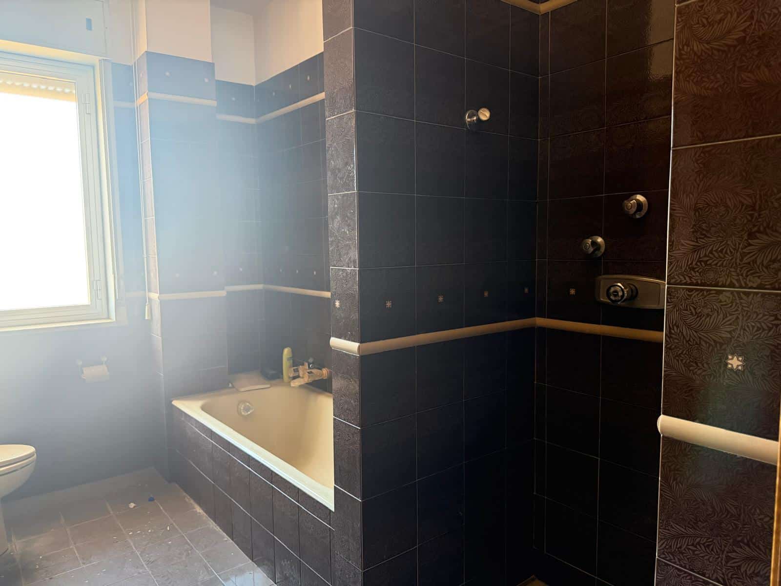 Il bagno moderno con vasca e doccia a pioggia, rivestito in piastrelle nere e dettagli in bianco, offre un ambiente elegante e funzionale, ideale per il comfort quotidiano.
