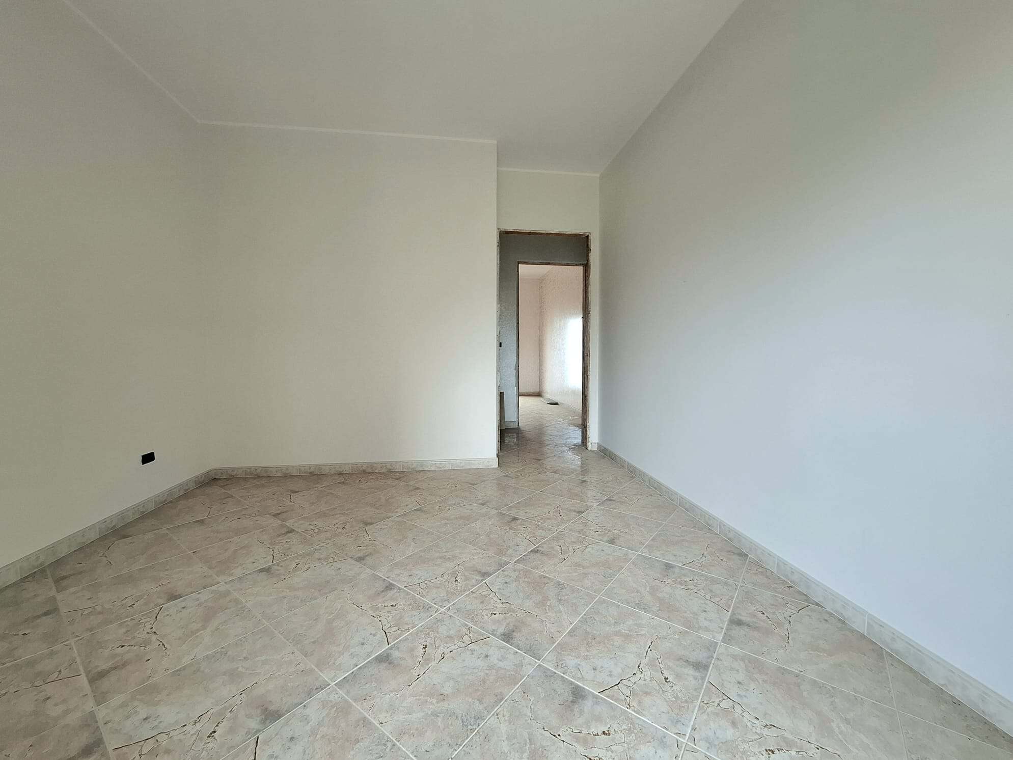 Ampia stanza vuota con pareti bianche e pavimento in piastrelle beige, pronta per essere arredata e personalizzata.