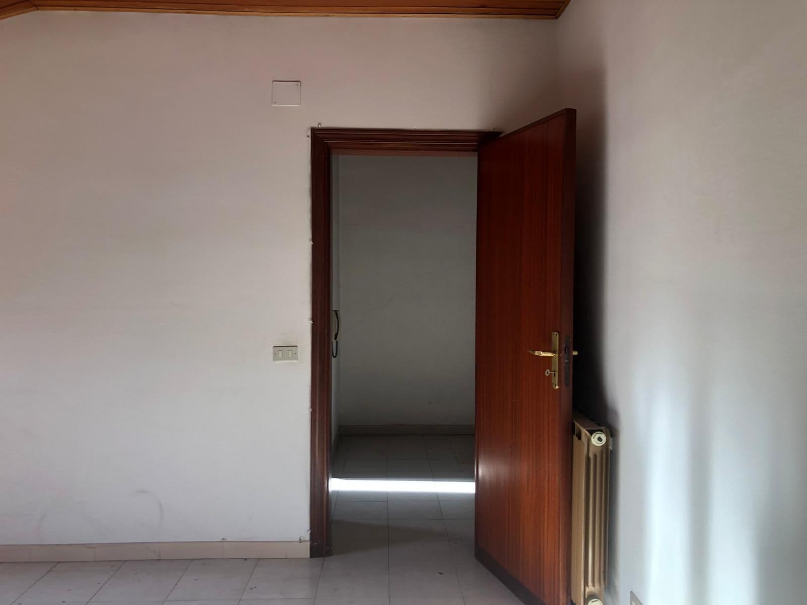 Porta in legno aperta in una stanza vuota con pareti bianche e radiatore, ambiente luminoso e semplice.