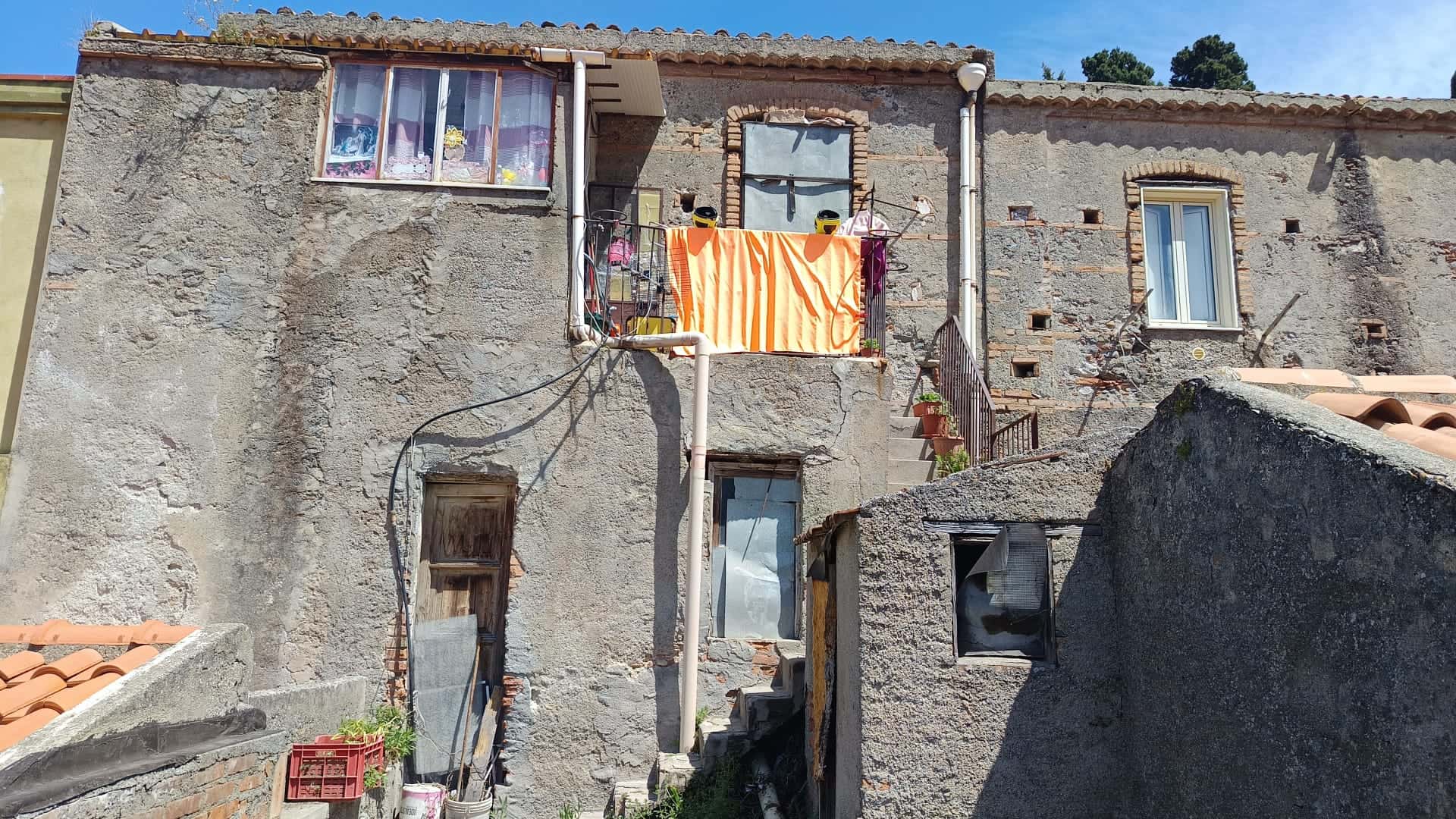 Panni stesi ad asciugare su un balcone di un edificio antico in stile rustico, con pareti in pietra e finestre con infissi in legno, in un contesto di quartiere storico italiano.