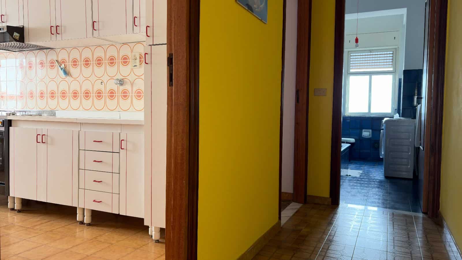 Ampia cucina moderna con mobili bianchi e dettagli rossi, pavimento in legno chiaro, ideale per vivere momenti conviviali e preparare pasti in famiglia o con amici.