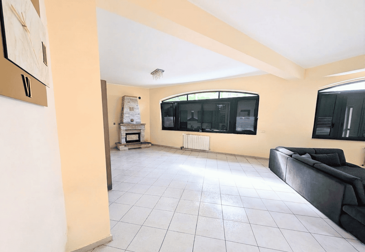 Interno spazioso di un appartamento con grandi finestre, camino e zona soggiorno con divano nero, ideale per affitti turistici o residenziali a NextCasa.