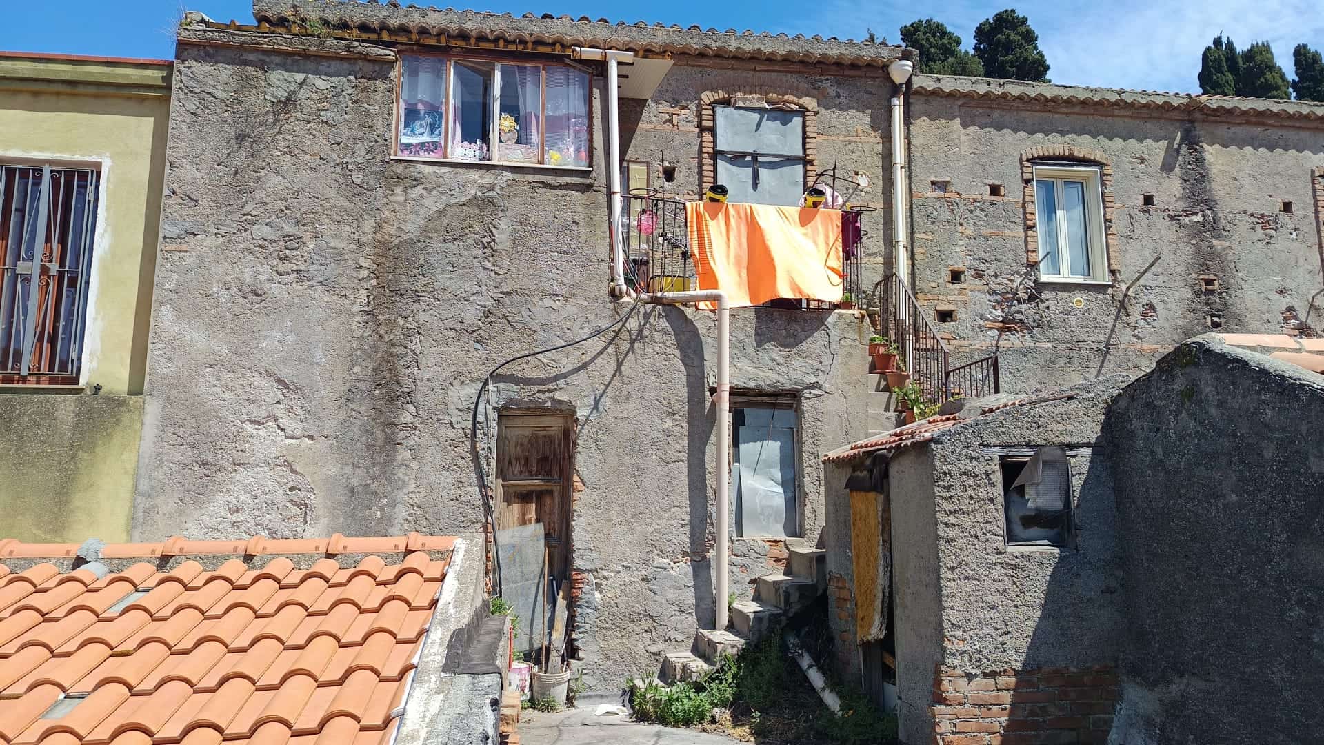 Antico edificio residenziale in pietra con balcone e tende arancioni, situato in un quartiere storico di NextCasa, perfetto esempio di architettura tradizionale italiana.