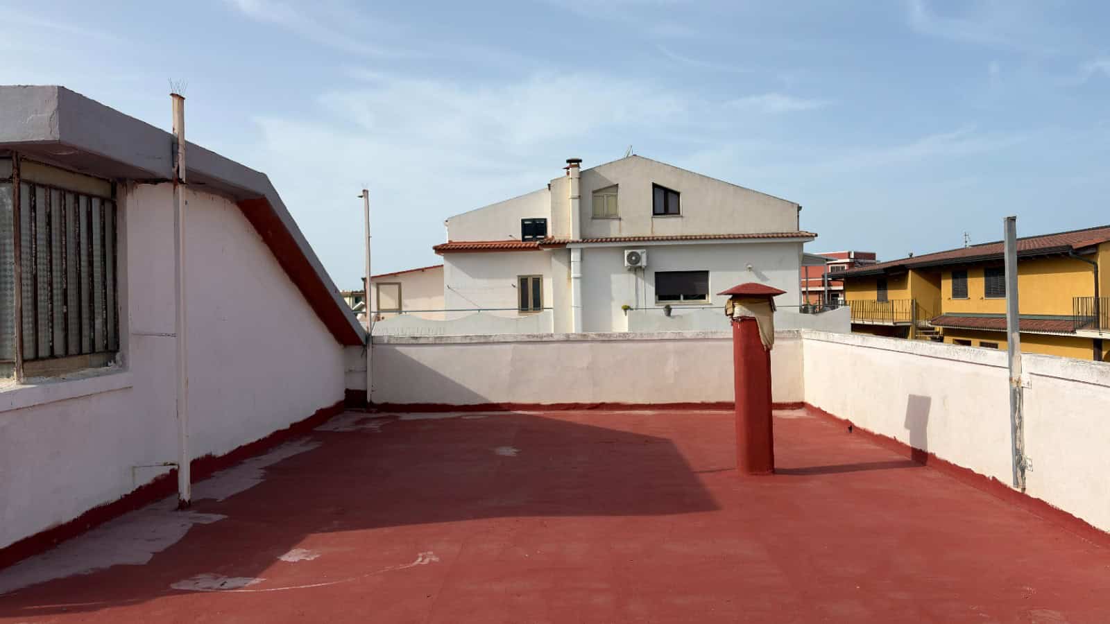 Tetto terrazza con superficie in resina rossa, vista su edifici residenziali e cielo sereno, ideale per relax e spazi all'aperto.