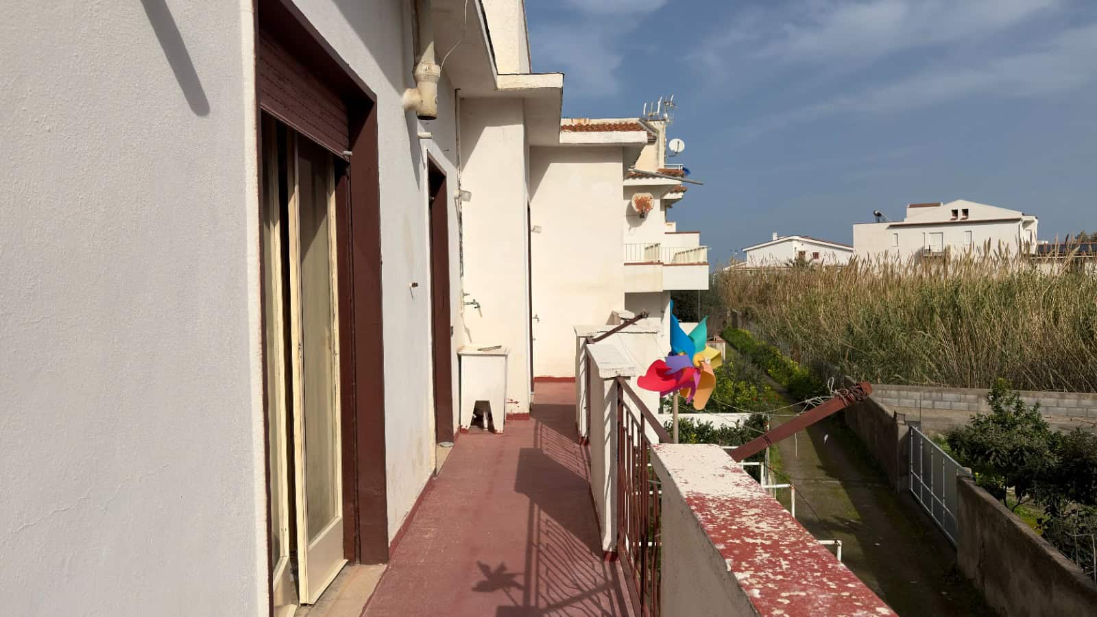 Balcone di un appartamento con vista su aree verdi e case moderne, in un contesto residenziale tranquillo, con accesso diretto e spazio per piante e decorazioni esterne.
