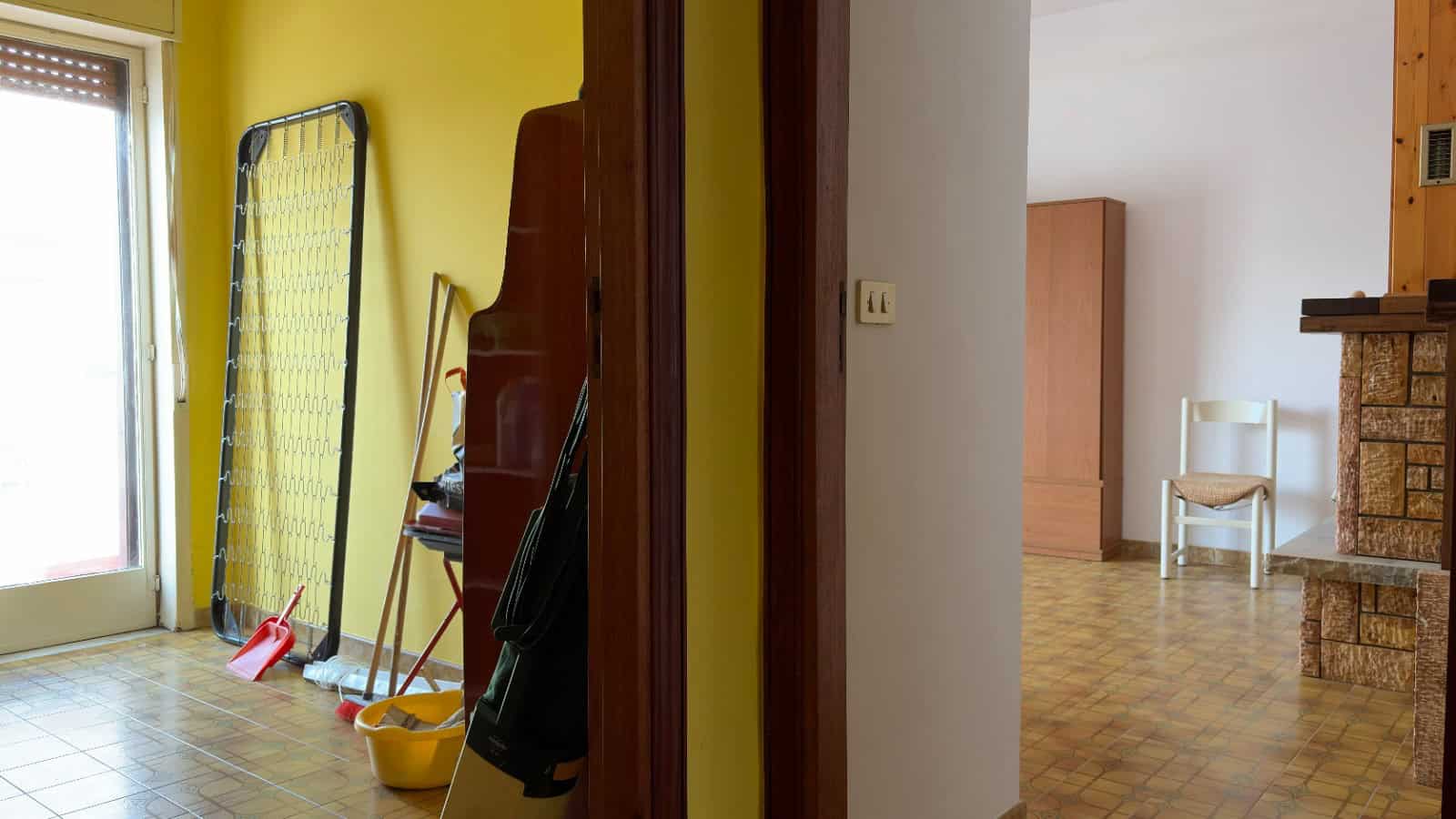 Spazzatura e attrezzi per la pulizia lasciati in un angolo di una stanza, con pareti gialle e pavimento in piastrelle, in un ambiente domestico in fase di riorganizzazione o pulizia.
