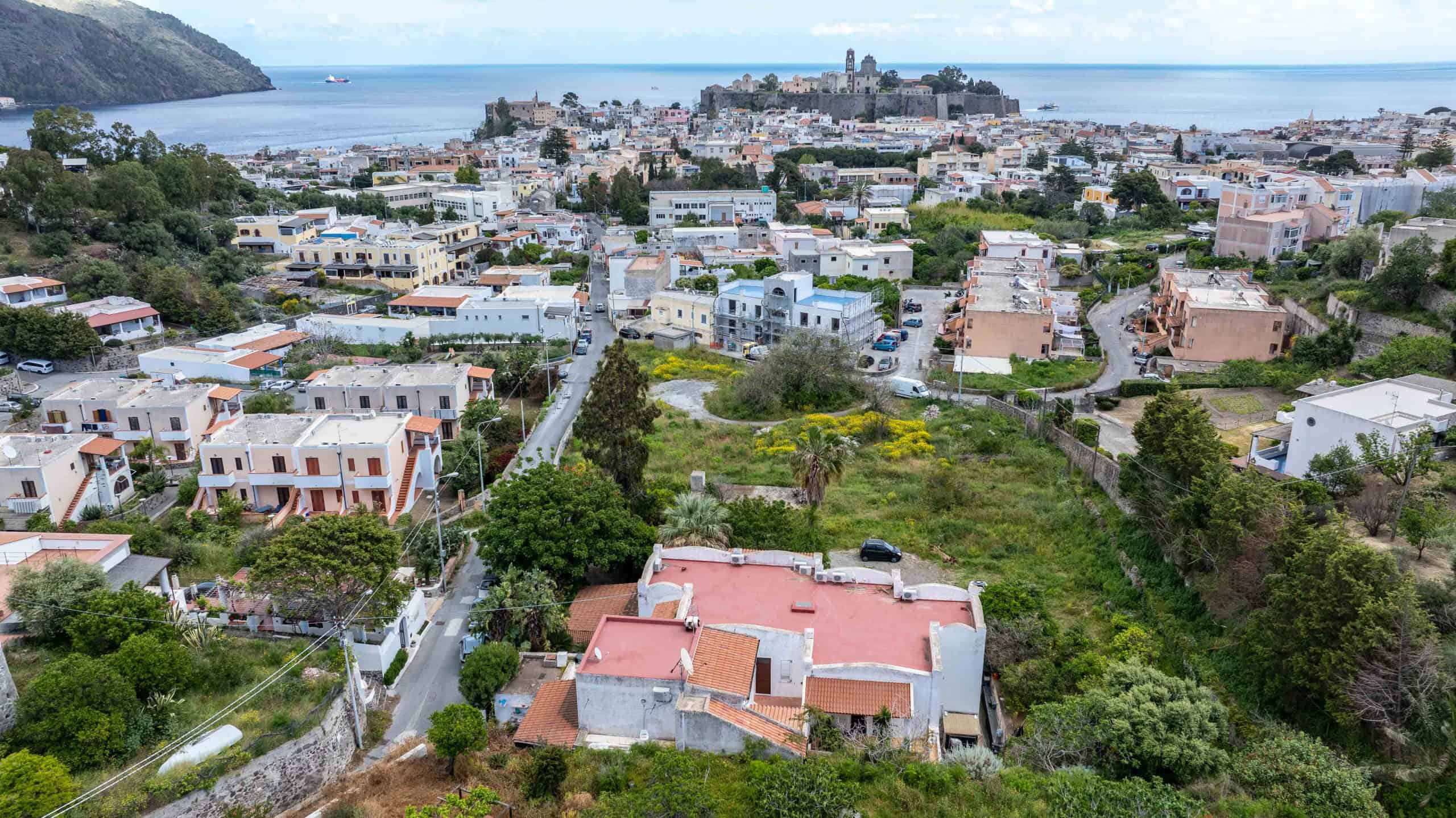 Vista panoramica di un quartiere residenziale con case colorate e vegetazione rigogliosa, sullo sfondo il mare e il centro storico di una città costiera italiana.