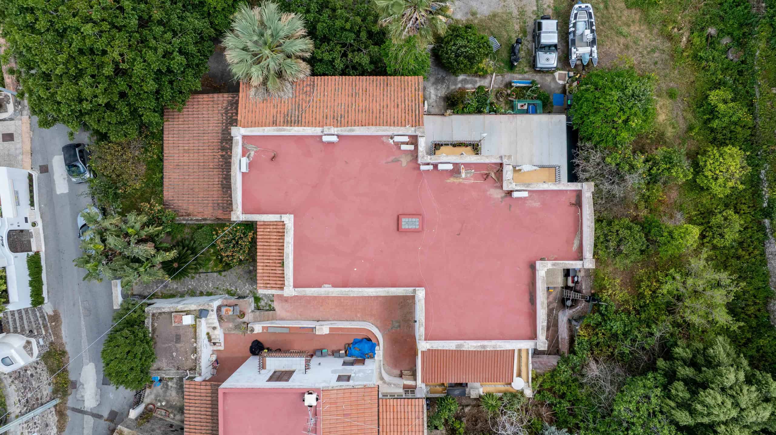 Ampio tetto rosso di una casa residenziale circondata da alberi e vegetazione, vista dall'alto, con alcune auto parcheggiate nelle vicinanze.