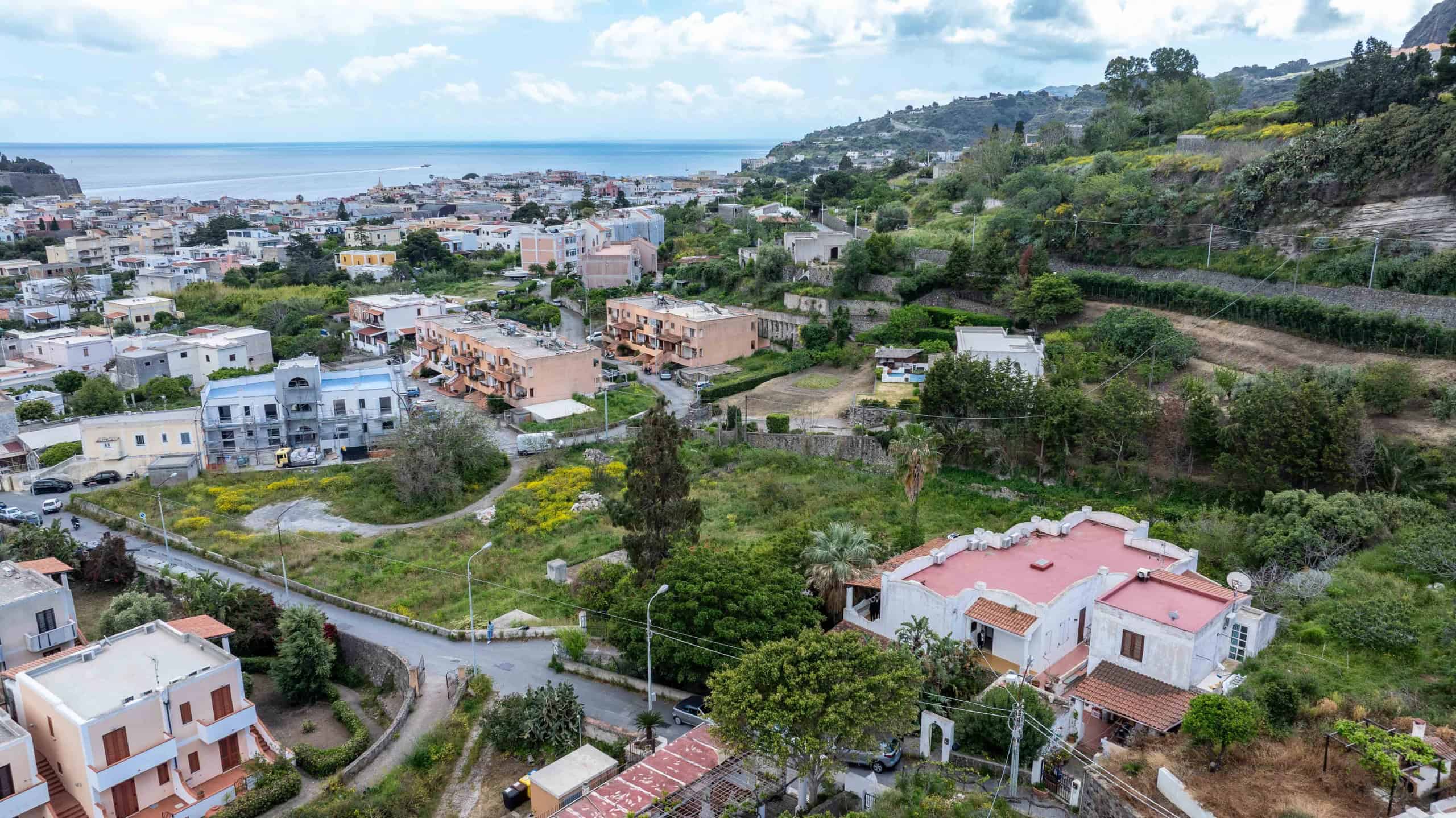 Vista panoramica di case residenziali e verdeggianti colline con vista mare in background, in un quartiere tranquillo e ben curato, con strade e giardini ben mantenuti, in una zona panoramica e solegg.