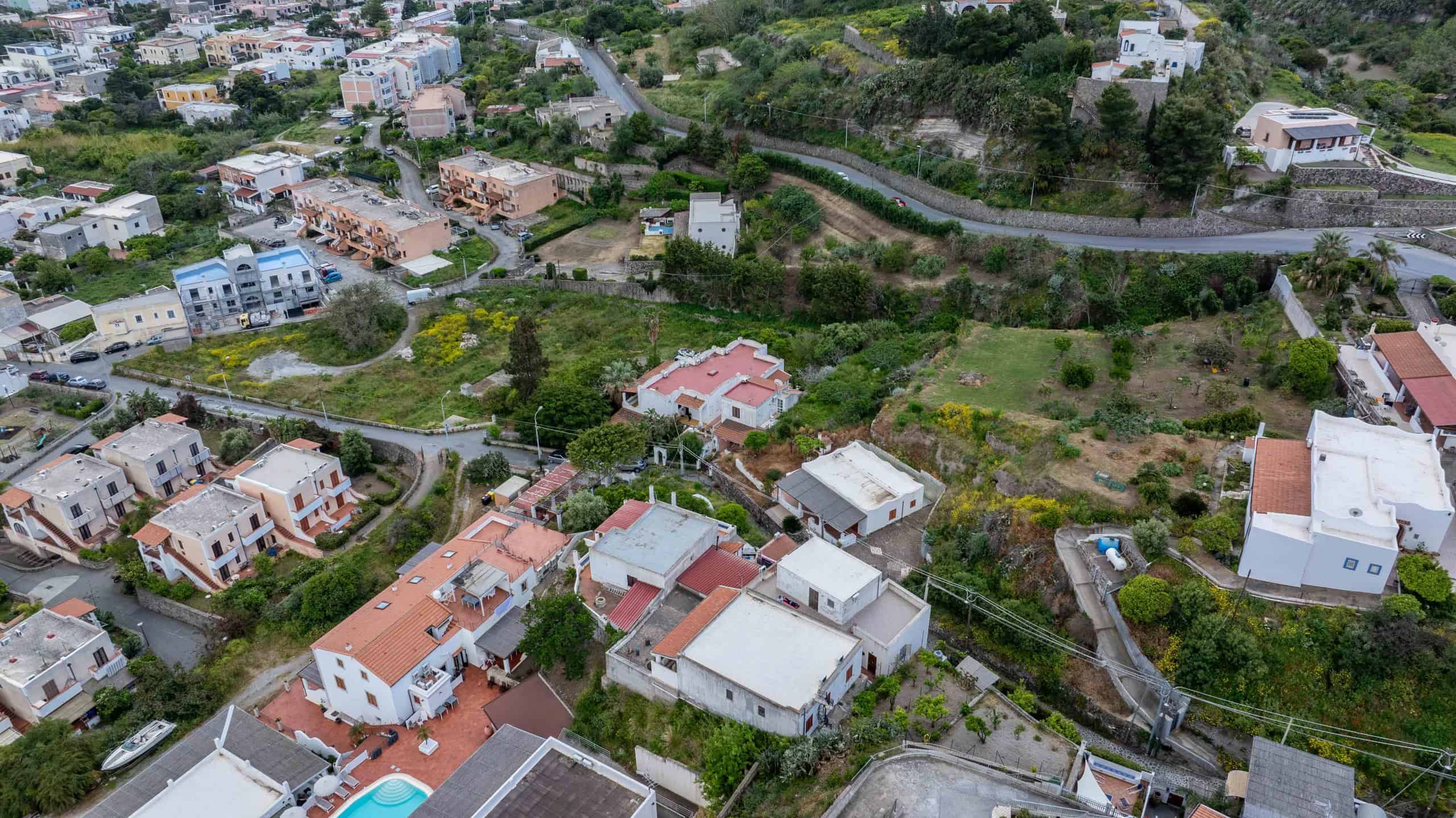 Immagine aerea di un quartiere residenziale con case moderne e strade sinuose, circondata da vegetazione e colline verdi, rappresentando un'area tranquilla e ben sviluppata in un contesto urbano natur.