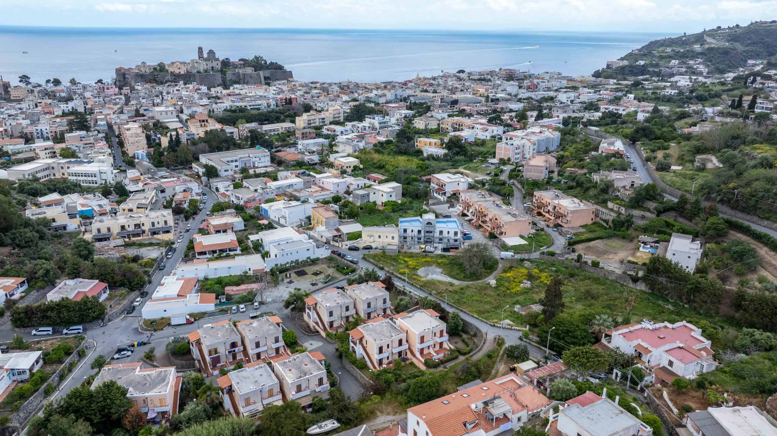 Vista panoramica di un quartiere residenziale a Napoli, con case colorate, strade e aree verdi, sullo sfondo il mare e il golfo, rappresentando un ambiente urbano vivace e pittoresco.