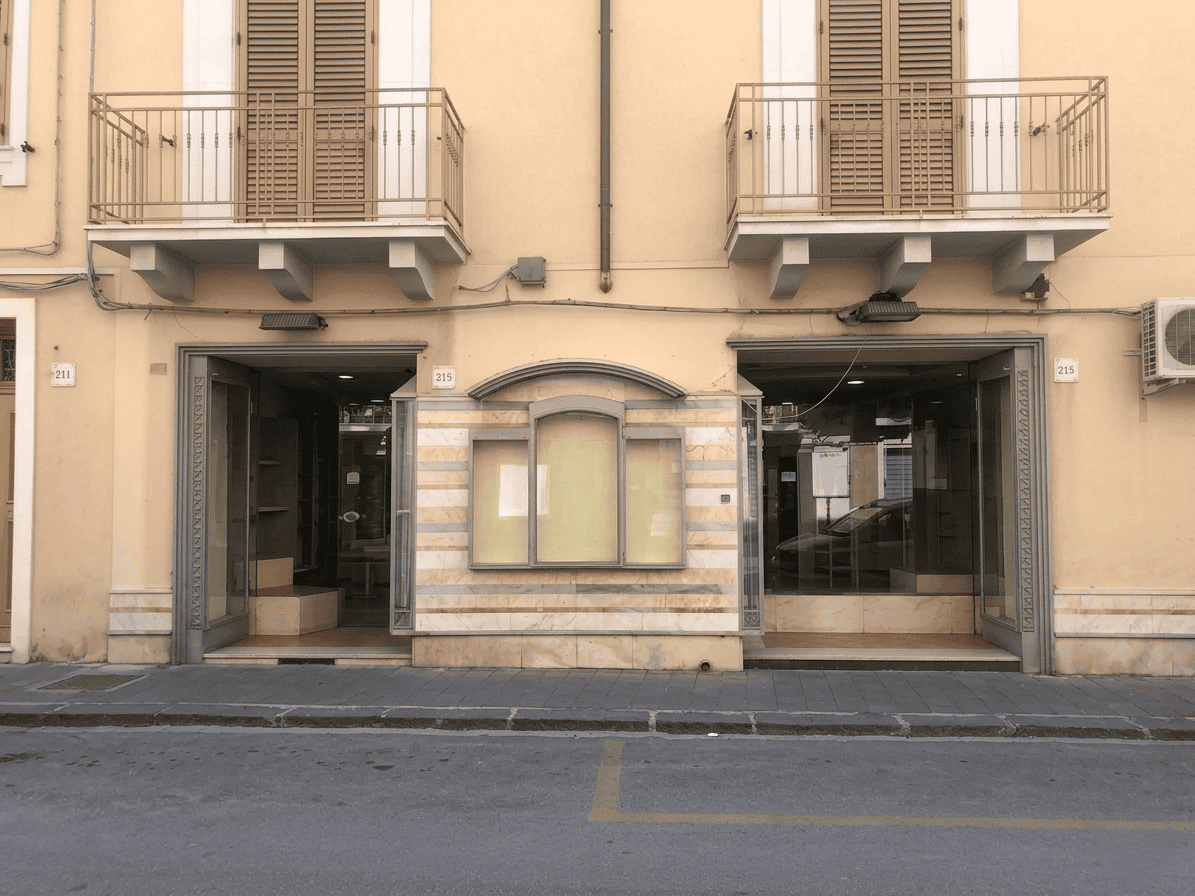Vetrina di negozio su strada con due ingressi e balconi al primo piano, edificio storico in stile italiano, facciata in pietra e dettagli architettonici eleganti.