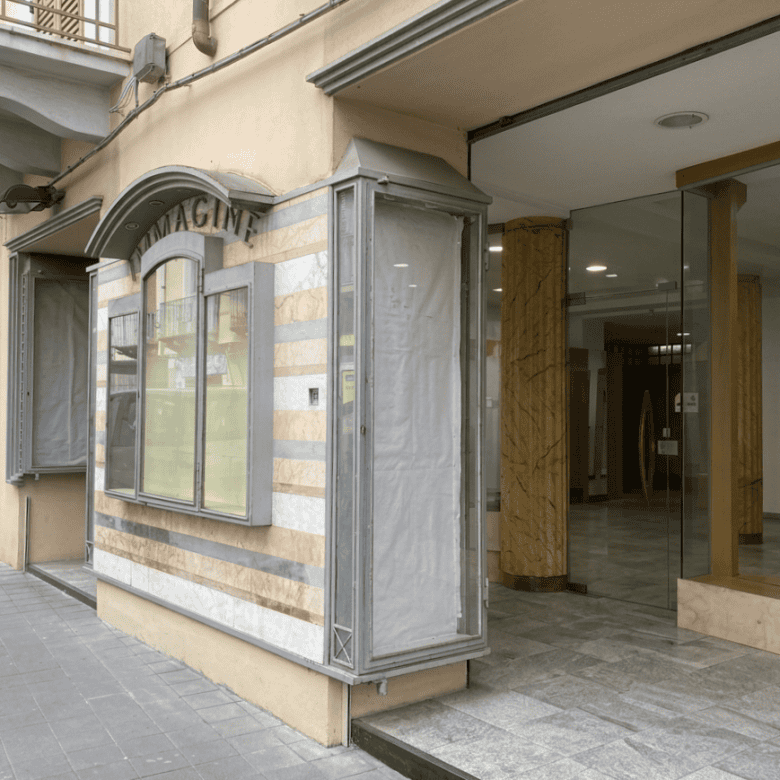 Vetrina e ingresso di un negozio con pareti in vetro e dettagli in metallo, situato in una strada urbana.