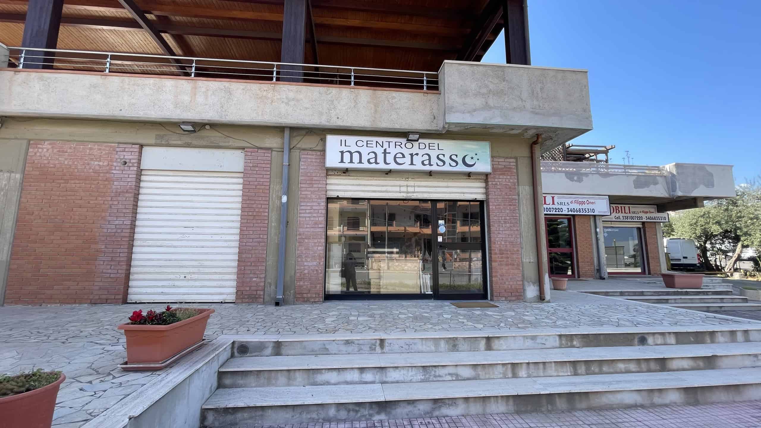 Il centro bed & breakfast Materassc, ingresso con scale e vetrina, in un edificio moderno con facciata in mattoni e cemento, situato in una zona urbana soleggiata.